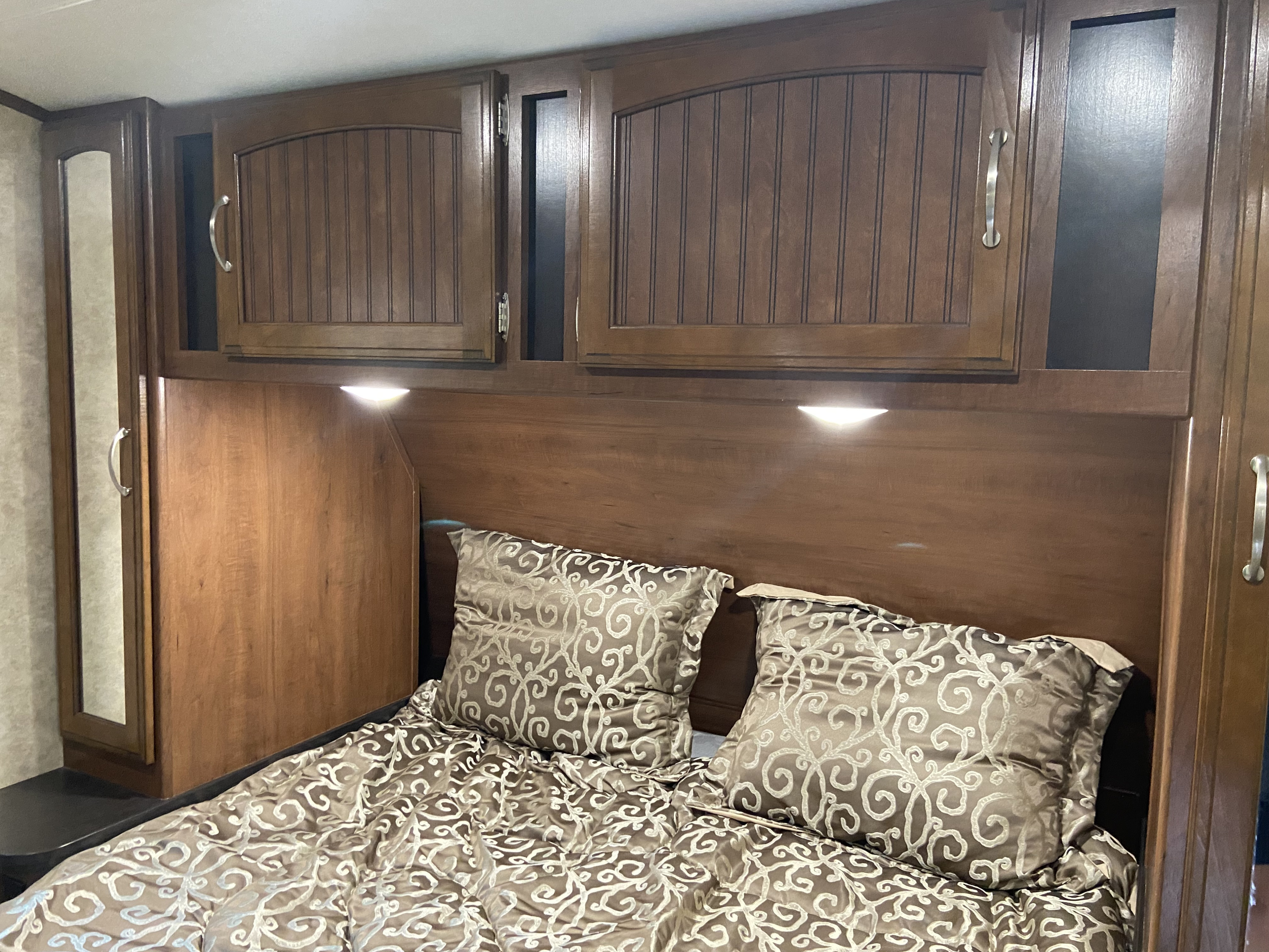 Cozy RV rental bedroom with ample overhead storage cabinets, reading lights, and a comfortable patterned bed.. Jayco White Hawk 2017