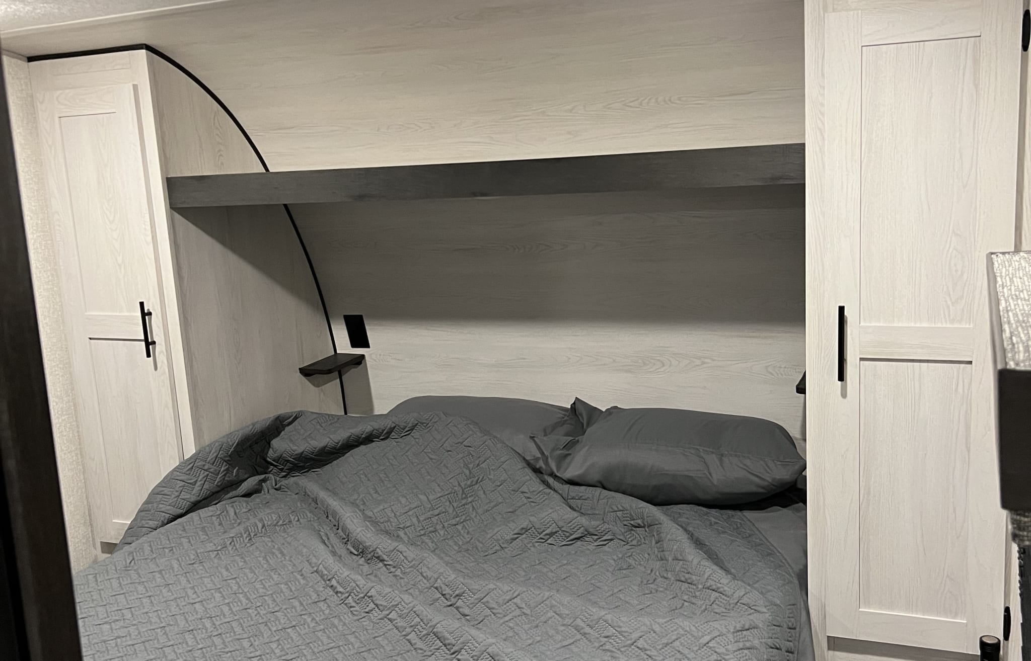 Cozy RV rental bedroom with light woodgrain cabinets, gray bed, and overhead shelf.. KZ Sportsmen 26BHSE 2022