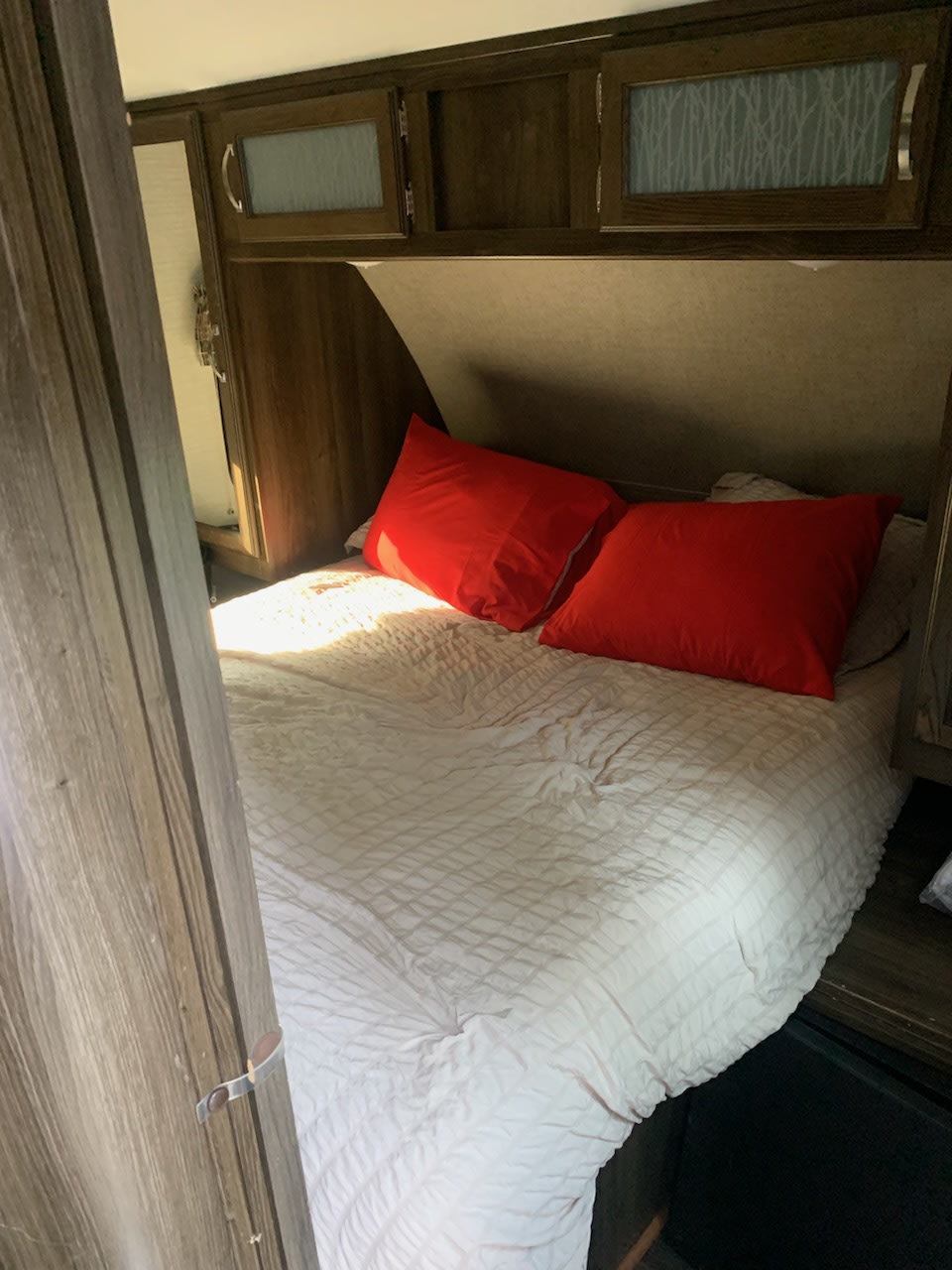 Inside an RV rental: a cozy bedroom features a bed with white comforter, bright red pillows, and overhead storage cabinets.. Keystone RV Bullet Ultra Lite 2018