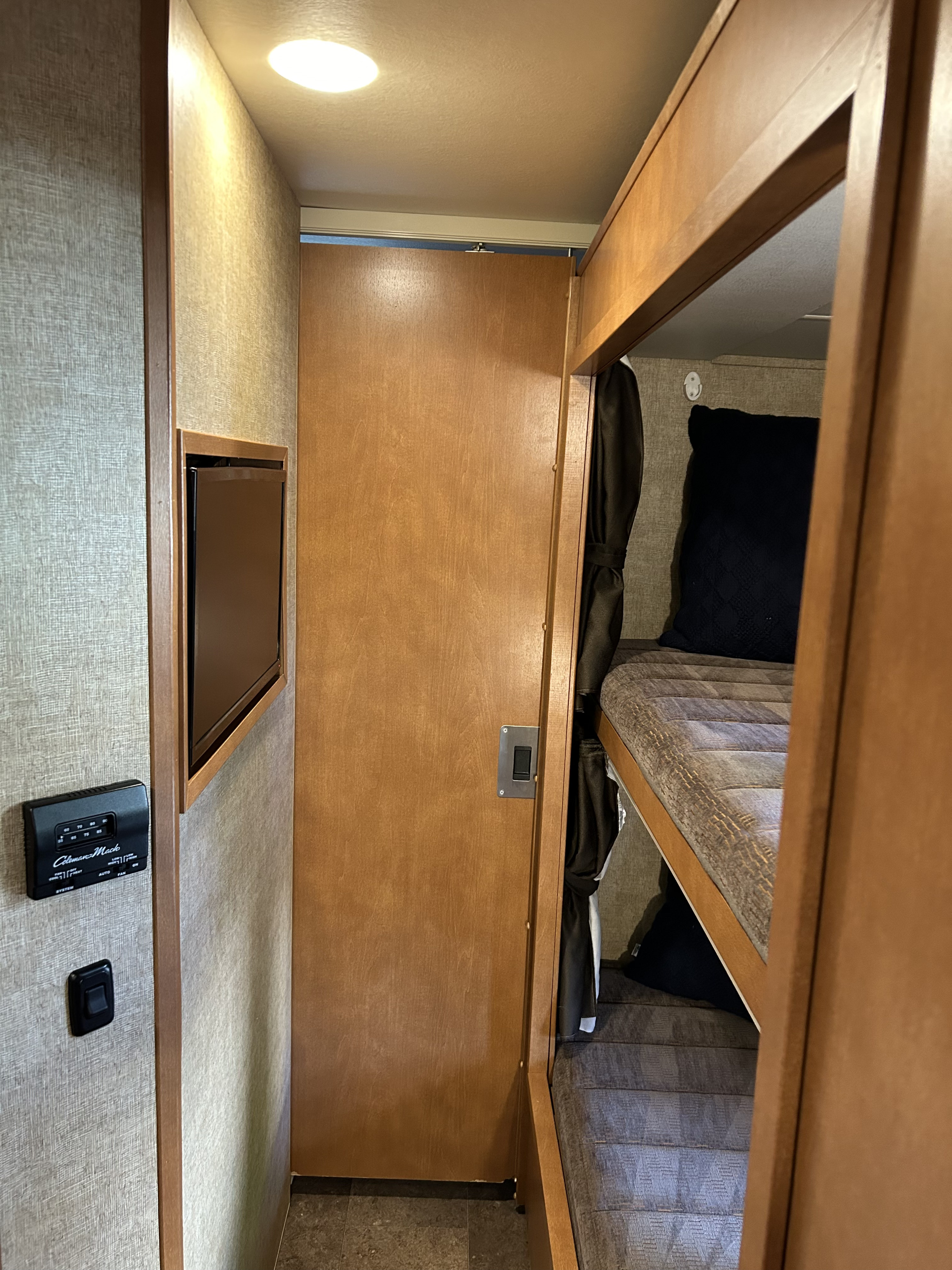 Inside an rv rental: A view of bunk beds with a dark pillow, a light wood door, a wall-mounted TV, and a thermostat.. Winnebago Minnie Winnie 2017