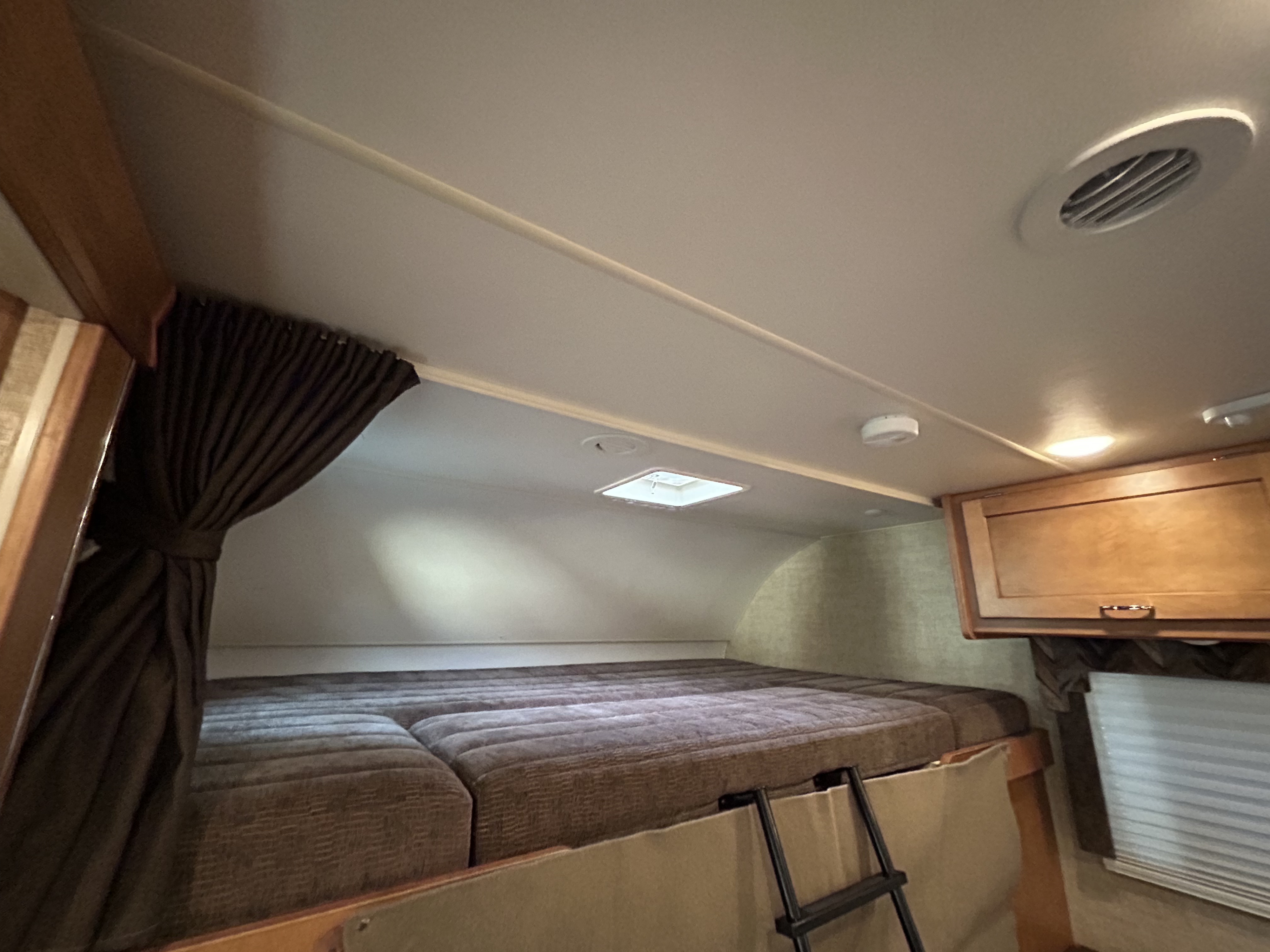 An RV rental's cozy interior features a large overhead bed, access ladder, curtains, and cabinets, ready for your adventure.. Winnebago Minnie Winnie 2017