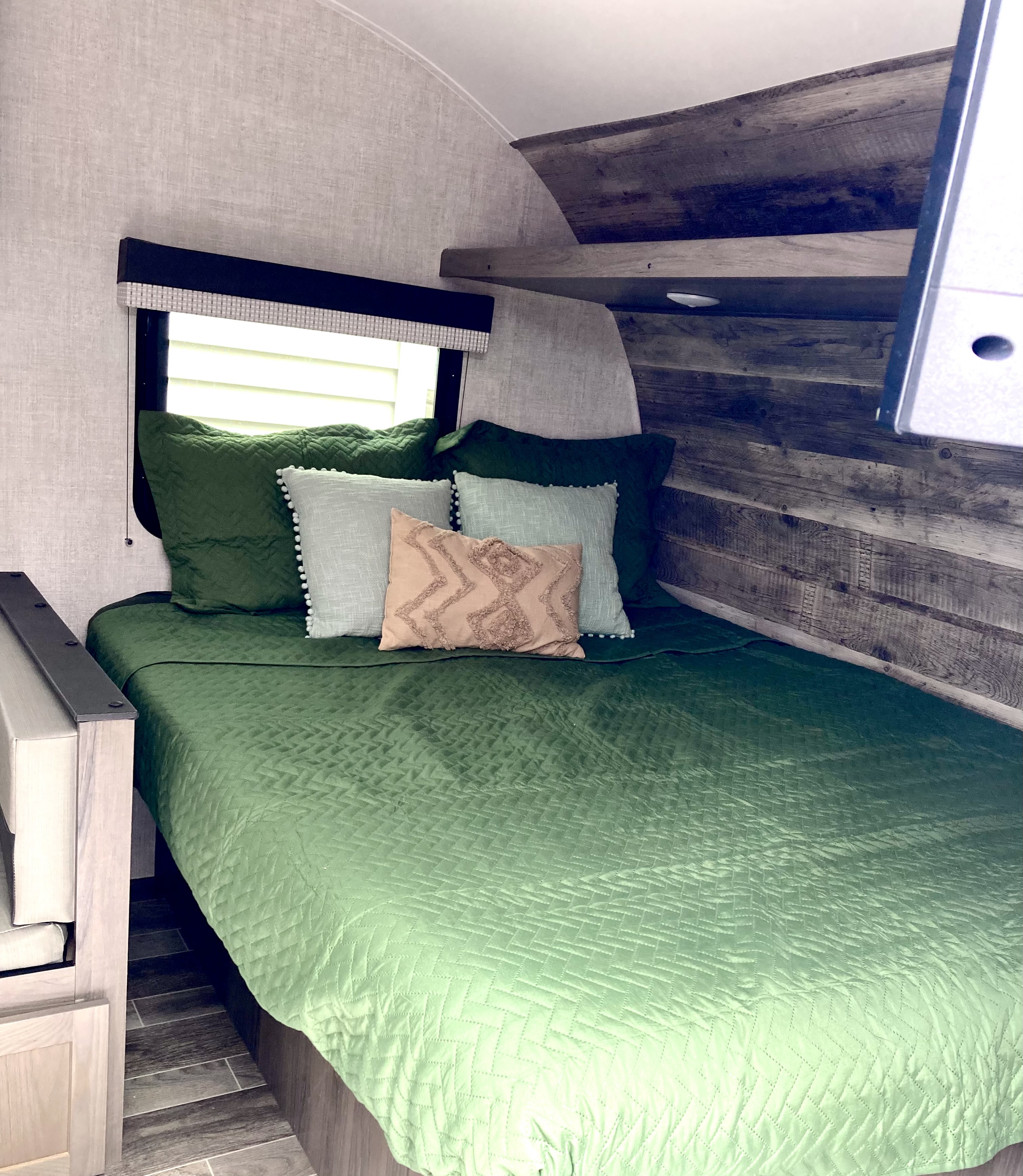 Cozy RV rental bedroom featuring a green bed quilt, decorative pillows, and rustic wood paneling, ready for travel.. Gulf Stream Ameri-Lite Super Lite 2022