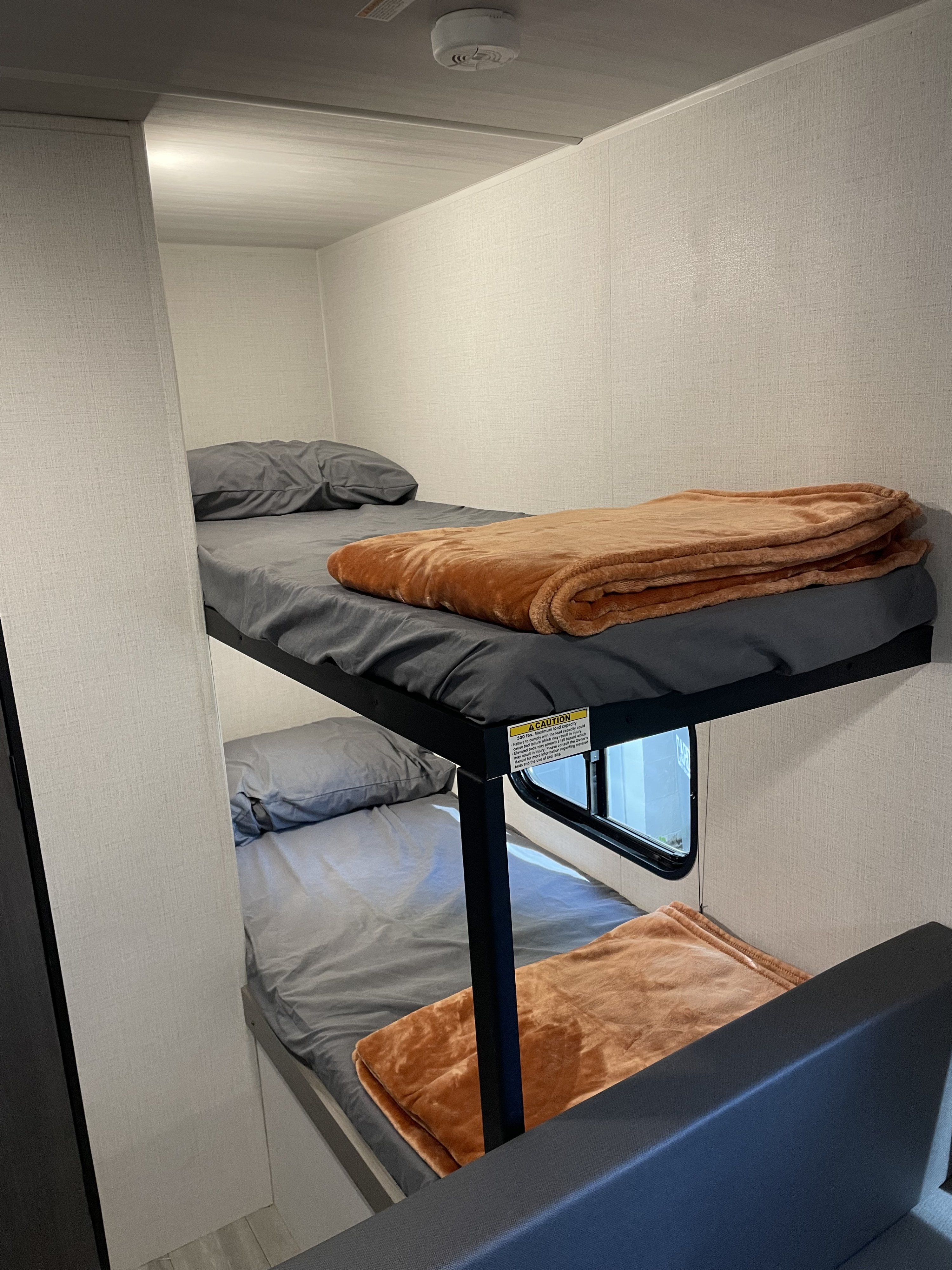 Inside an RV rental, two cozy bunk beds with gray sheets and orange blankets offer a compact sleeping area.. Keystone RV Hideout Sport 2024