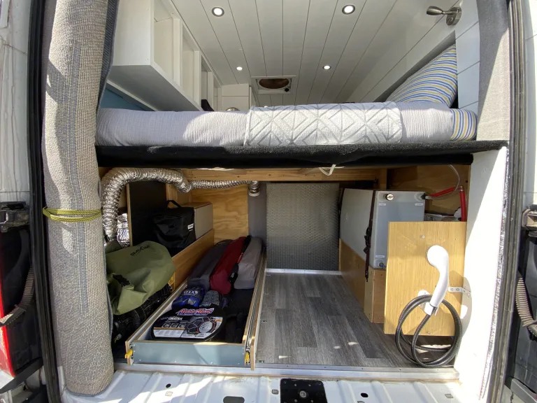 RV rental: Camper van's organized rear storage area. Raised bed above, utilities like a shower & water tank below.. Ford Transit Custom 2015