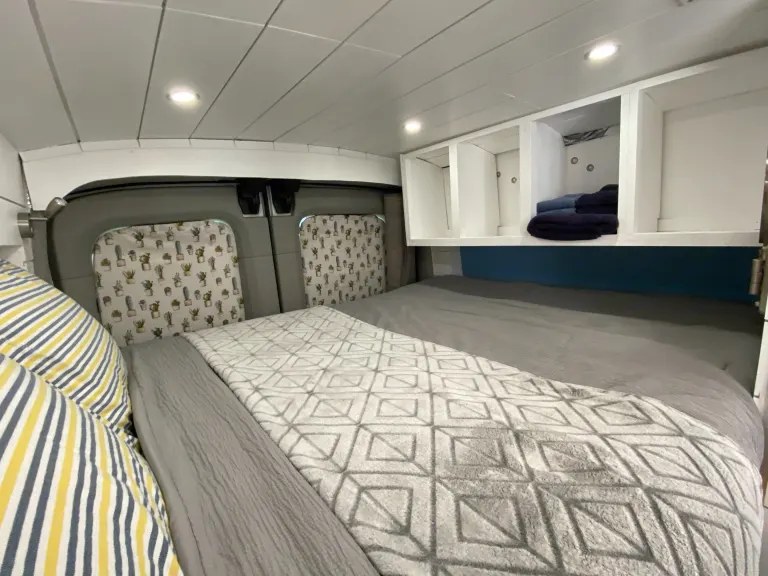 Cozy RV rental bedroom with a comfy bed, overhead storage, and fun cactus window covers.. Ford Transit Custom 2015