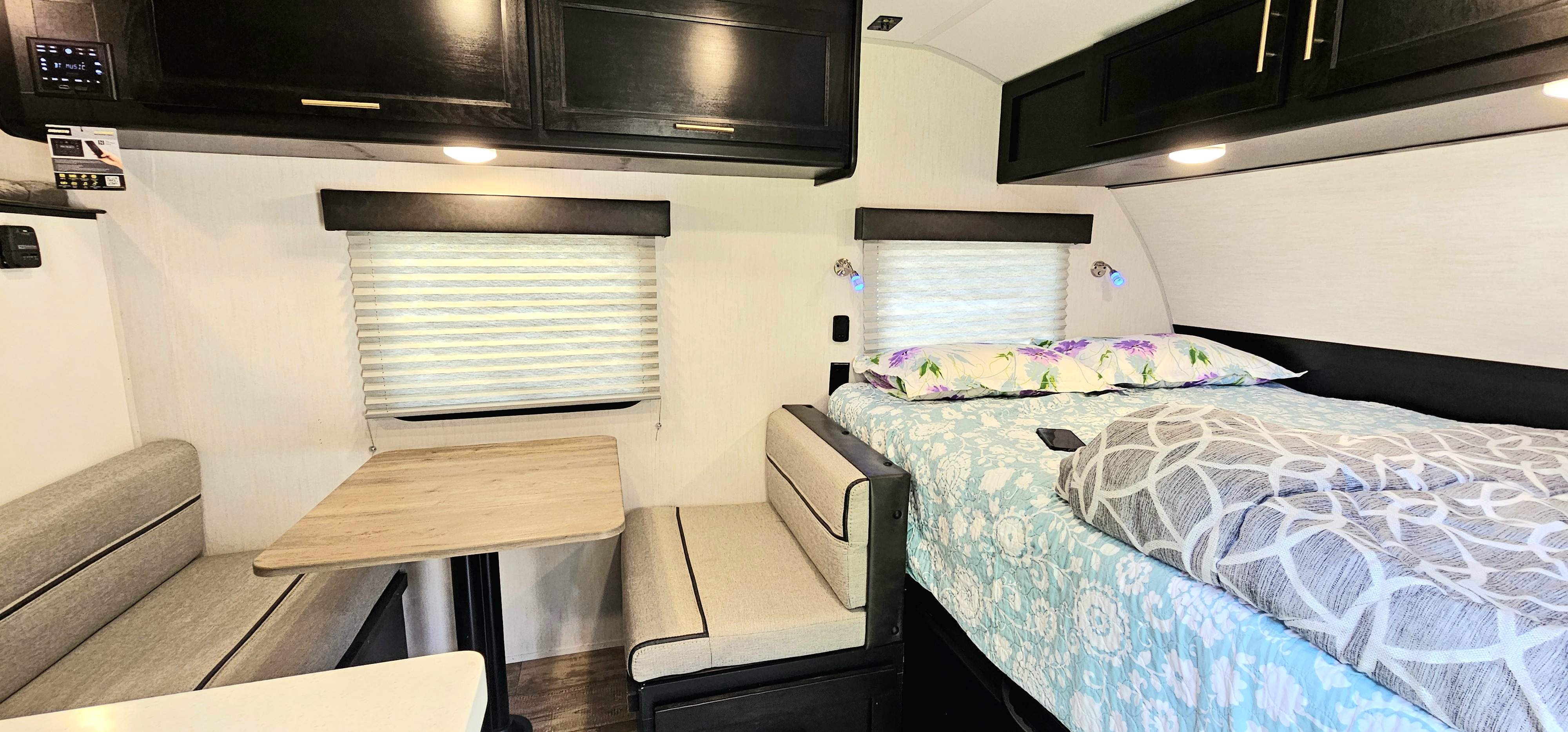 Cozy RV rental interior: a dinette booth with a table, overhead cabinets, and a comfortable bed with reading lights.. Forest River Cherokee Wolf Pup Black Label 2022