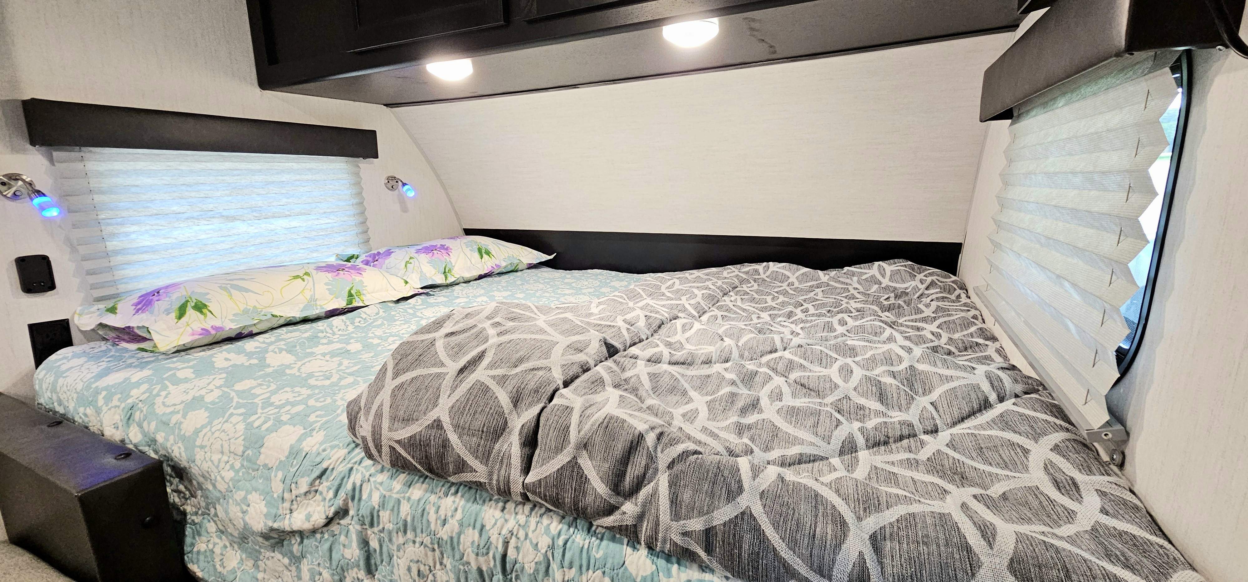 Comfortable RV bedroom interior, ideal for your rv rental getaway. Features a bed with patterned bedding, reading lights, and window blinds.. Forest River Cherokee Wolf Pup Black Label 2022