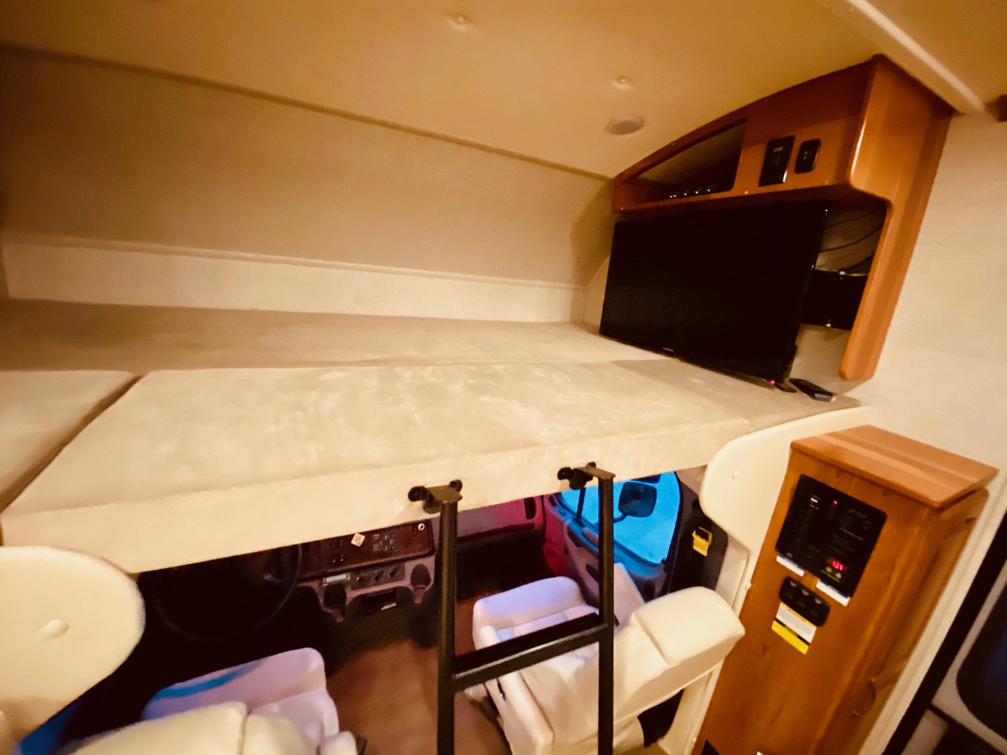 Interior view of an RV rental, showing the cab-over bunk, driver's cockpit below, TV, and system controls.. Jayco Seneca 2018