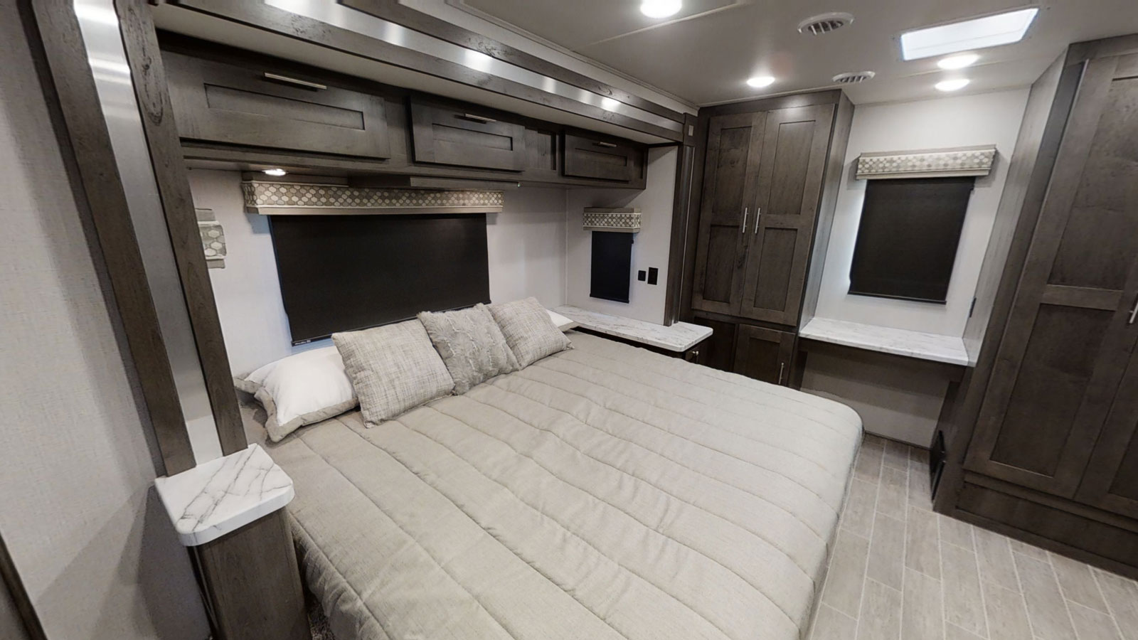 View of a modern RV rental bedroom with a large bed, stylish overhead cabinets, and functional built-in storage.. Forest River gt5 2021