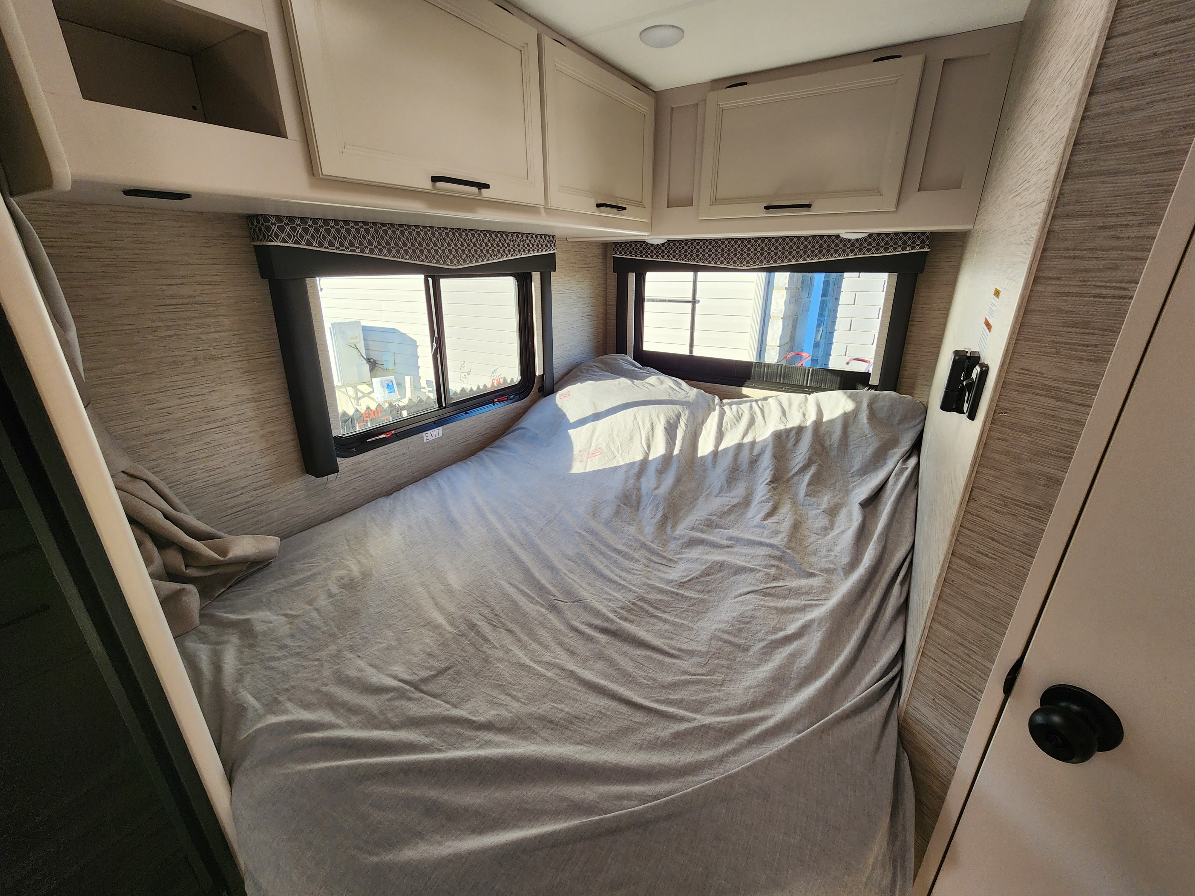 Cozy rv rental bedroom interior, featuring a light grey bed, bright windows, and beige overhead cabinets.. Thor Four Winds 2024