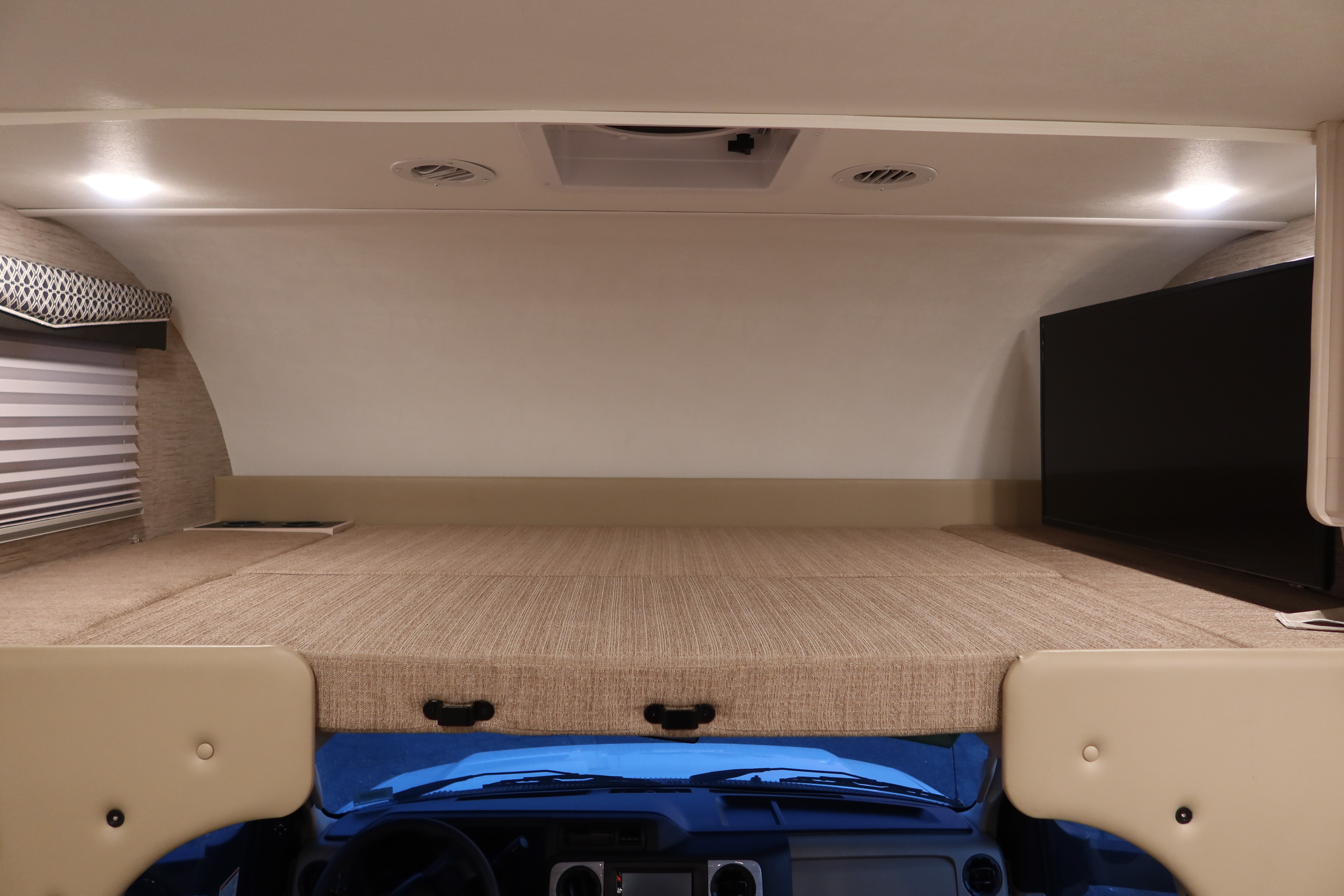 Inside an rv rental, featuring a spacious cab-over bunk bed. Includes window blinds, a TV, and overhead lighting for comfort.. Thor Motor Coach Chateau 27R 2022