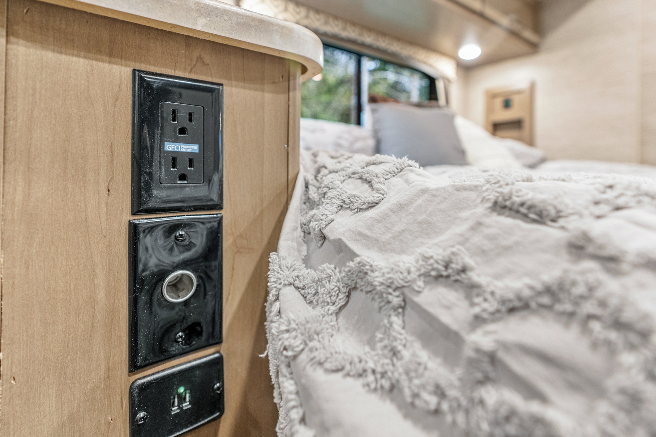 Stay charged in your RV rental bedroom! Close-up shows GFCI, 12V, and USB outlets beside a cozy bed.. Thor Motor Coach Chateau 27R 2022
