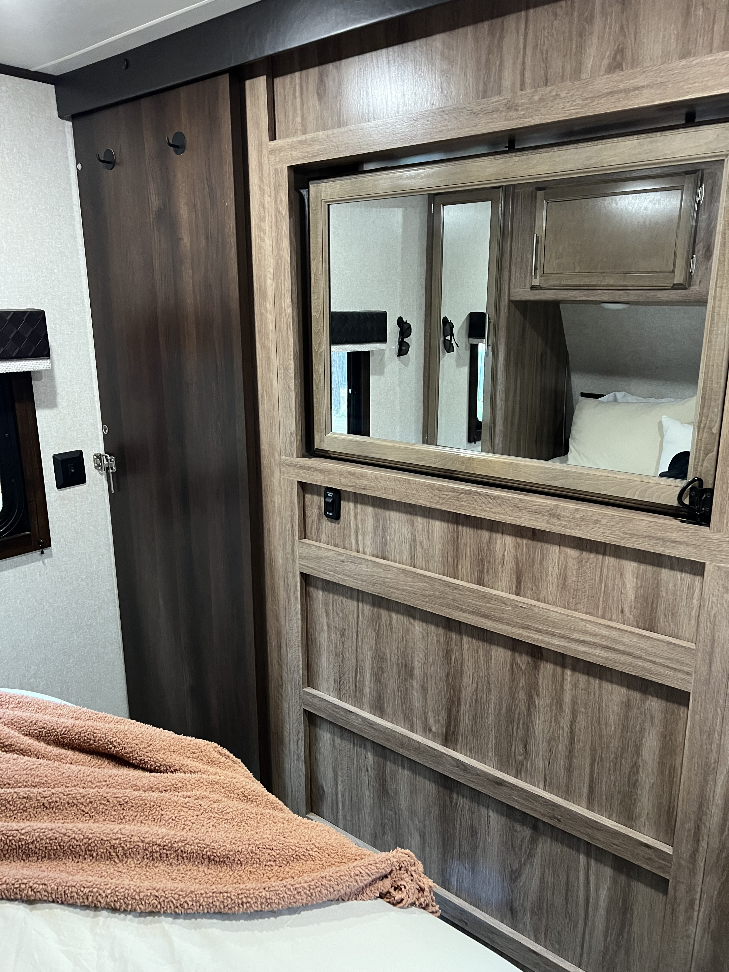 Inside an RV rental: a cozy bedroom with a peach blanket, dark wood closet, and mirrored cabinet.. Jayco Jay Feather 2019