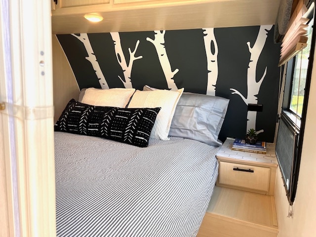 Modern RV rental interior features a cozy bedroom with striped bedding, patterned pillow, birch tree wall art, and a nightstand.. Winnebago Minnie Winnie 2016