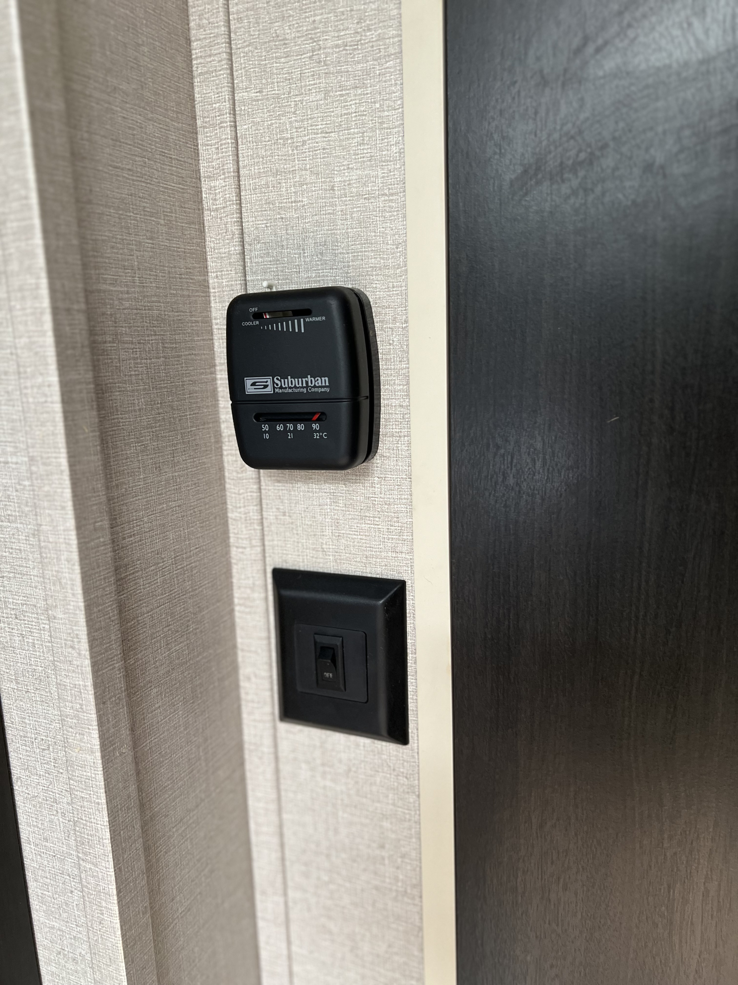 Inside an RV rental, showing a Suburban thermostat controlling temperature and a light switch for essential comfort controls.. Sonic Sonic Trailer 2019