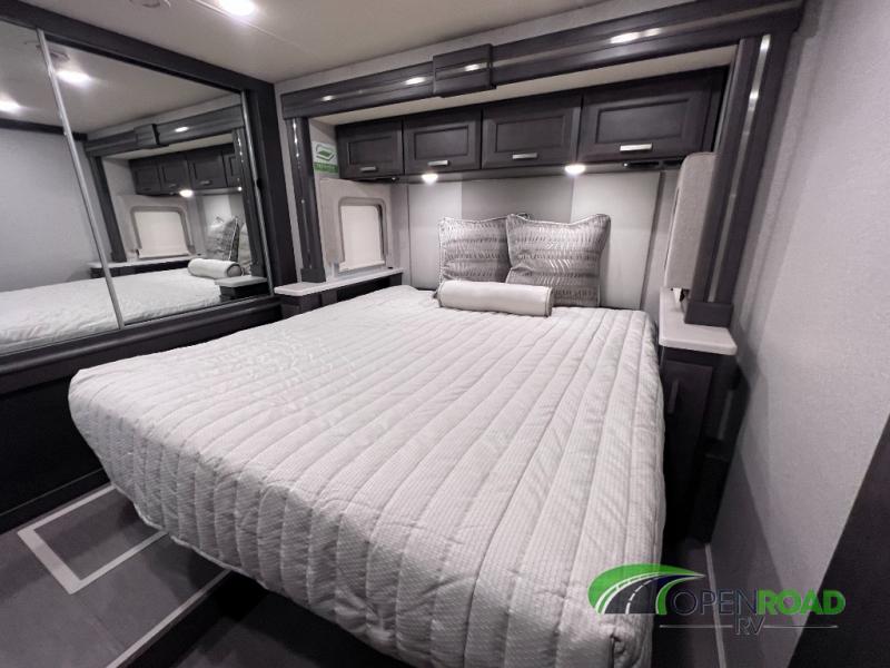 Explore a modern RV rental bedroom with a comfy bed, mirrored closet, and convenient overhead cabinets for travel.. Thor Palazzo 2023