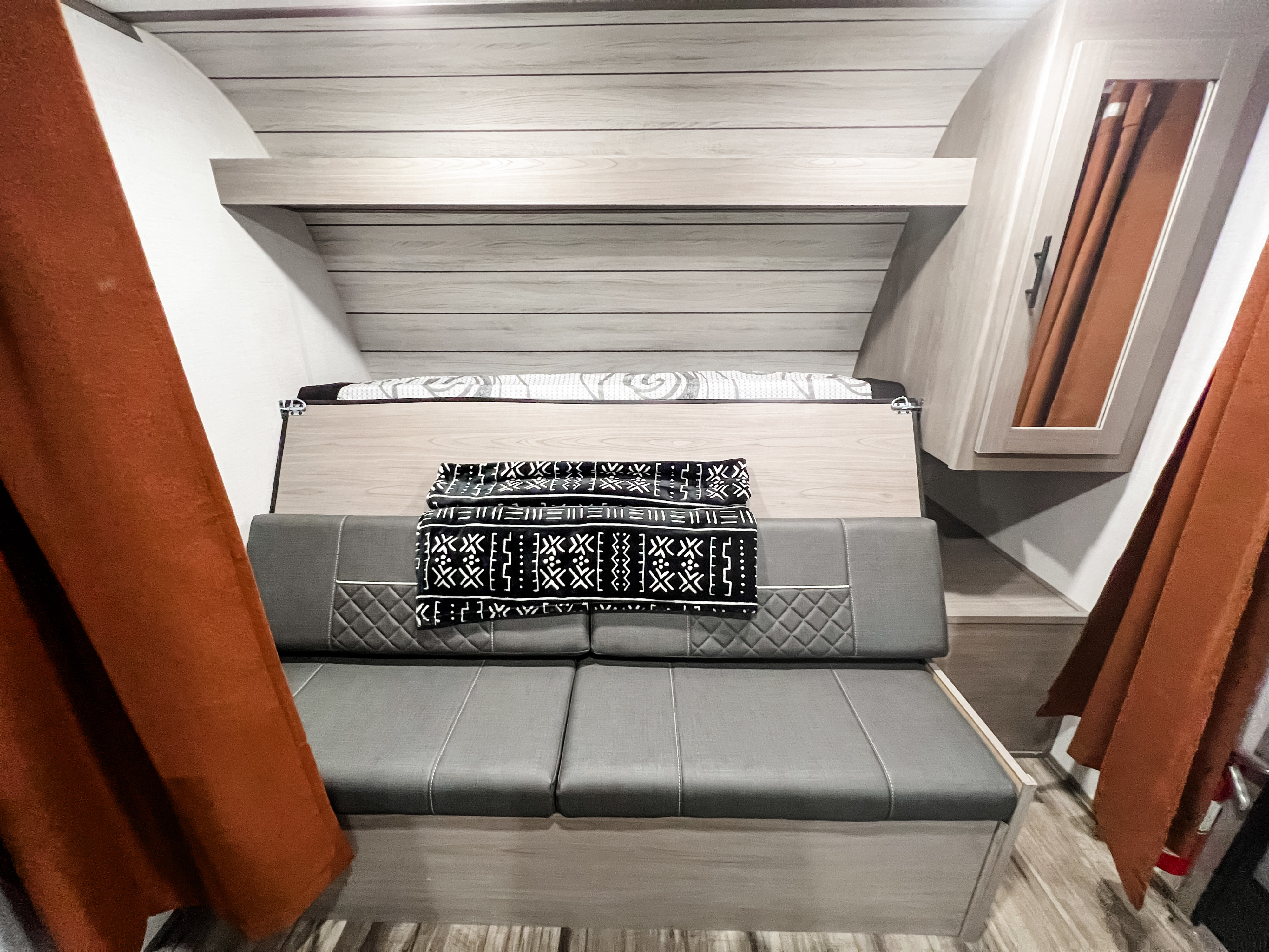 Comfortable **rv rental** interior showcasing a grey sofa, murphy bed, and modern wood finishes, framed by warm orange curtains.. Dutchmen Lantern LT BB19 2024