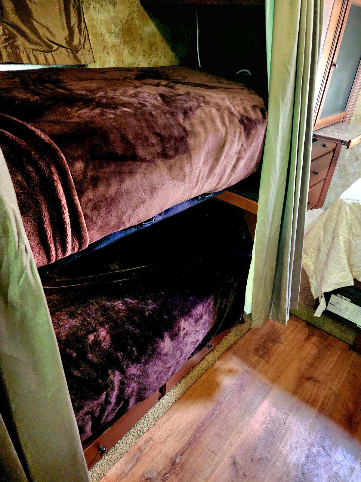 RV rental bunk beds: a compact sleeping area with plush dark blankets and privacy curtains on a wooden floor.. Tioga Ranger 2013