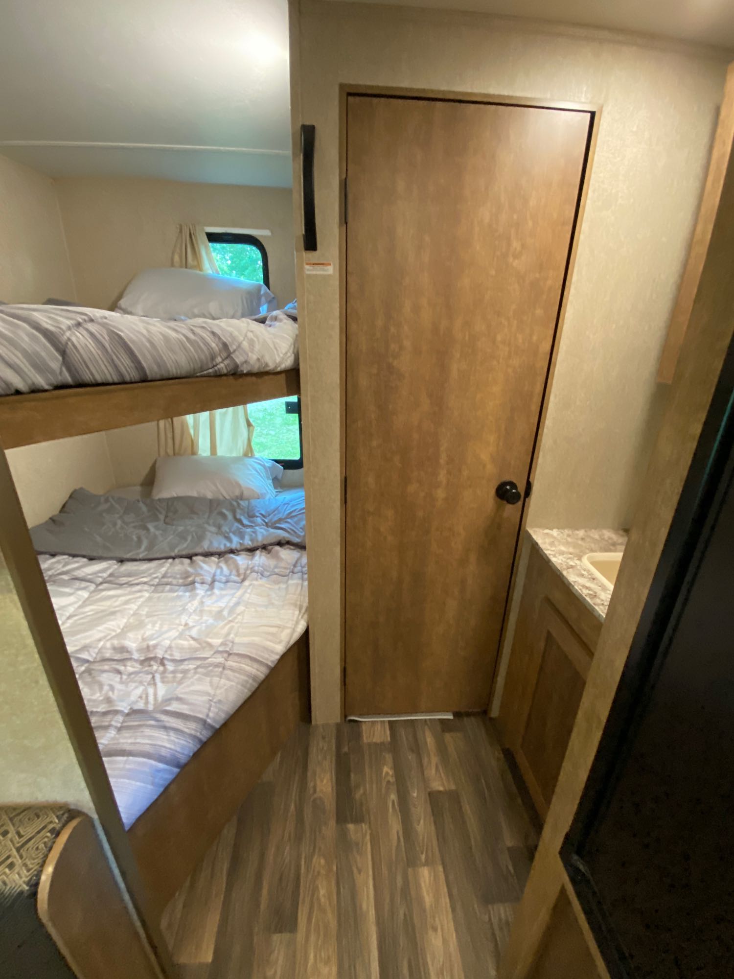 RV rental interior: bunk beds with bedding, a wooden door, and a compact bathroom with a sink. Wood-look floor. Ideal for small families.. Starcraft AR-One Maxx 2017