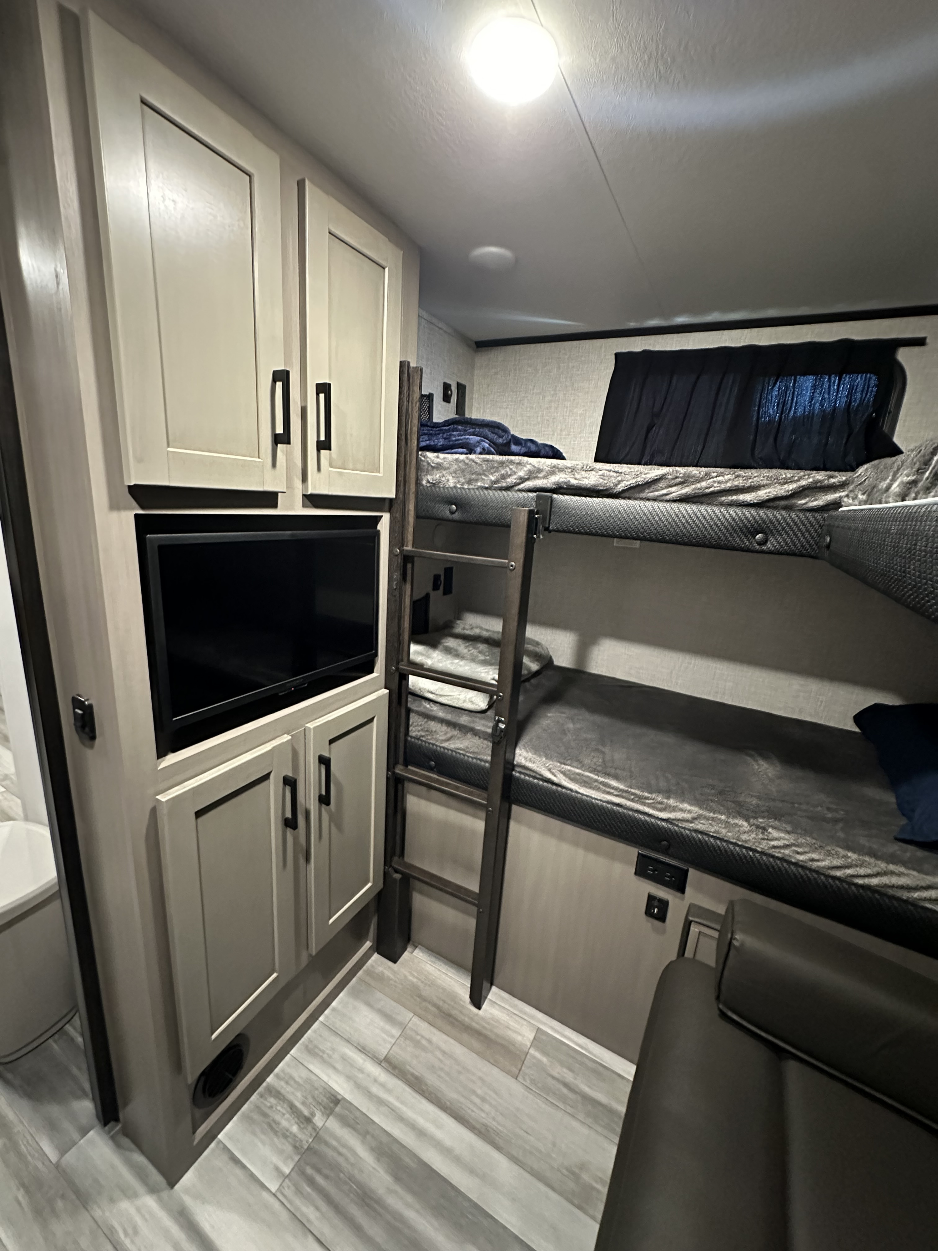 This RV rental interior reveals a compact space with bunk beds, a mounted TV below cabinets, and wood-look flooring.. Jayco Jay Feather 2024