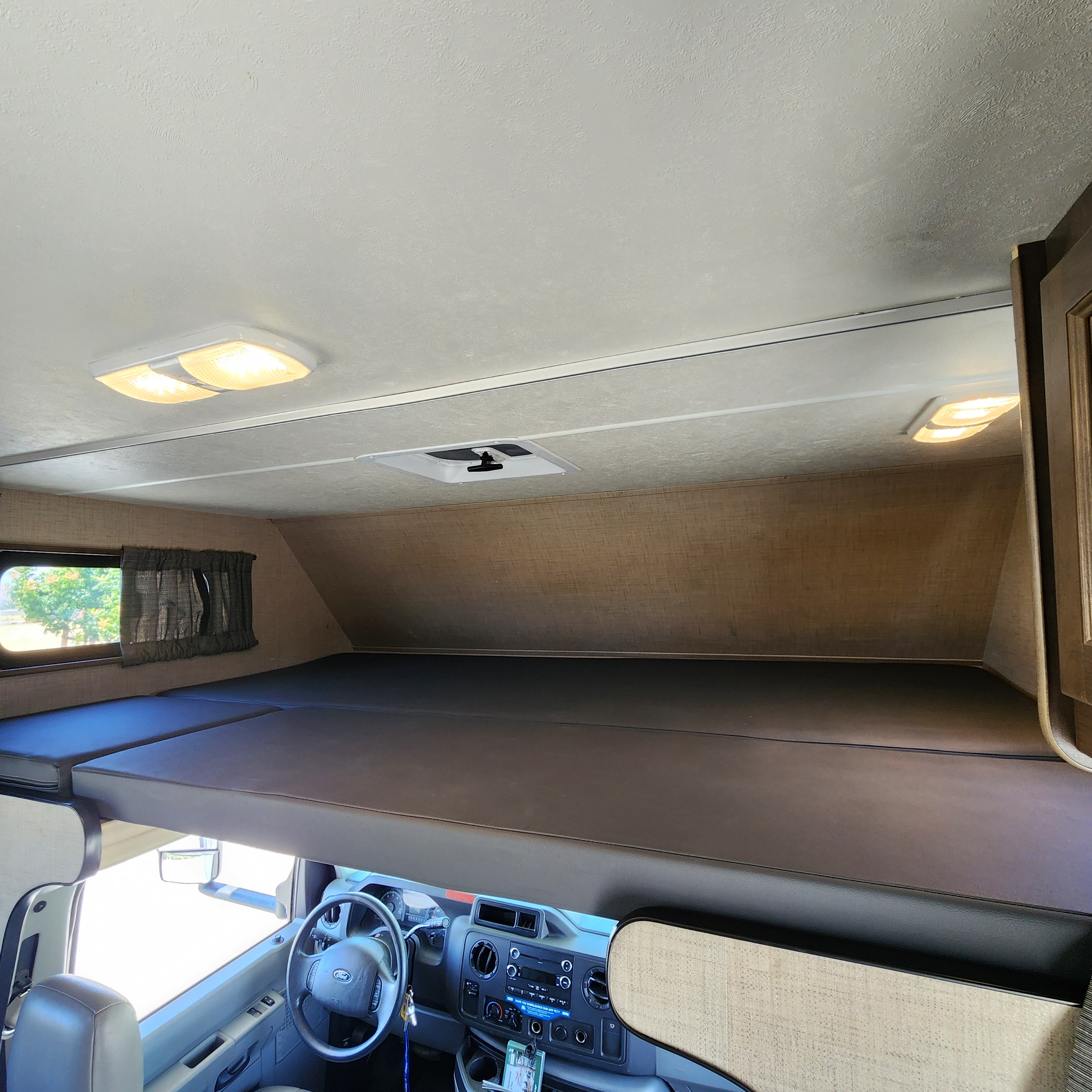 Inside this RV rental: a cozy cab-over bunk bed and the cockpit area with dashboard and steering wheel.. Thor Majestic 2019