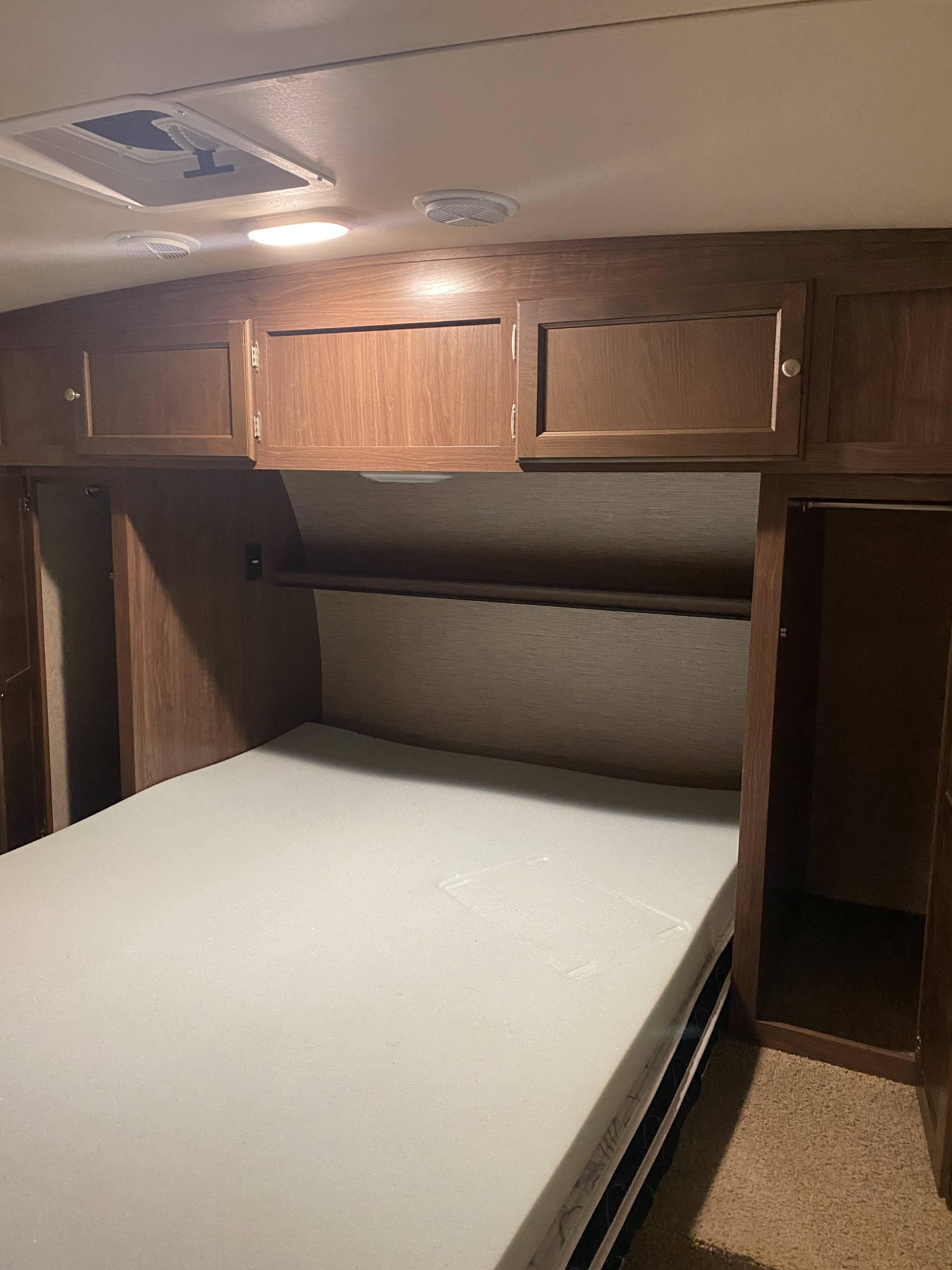 Cozy RV rental bedroom showing a white foam mattress, wooden overhead cabinets, a hanging rod, and ceiling fixtures.. Palomino Solaire 2015