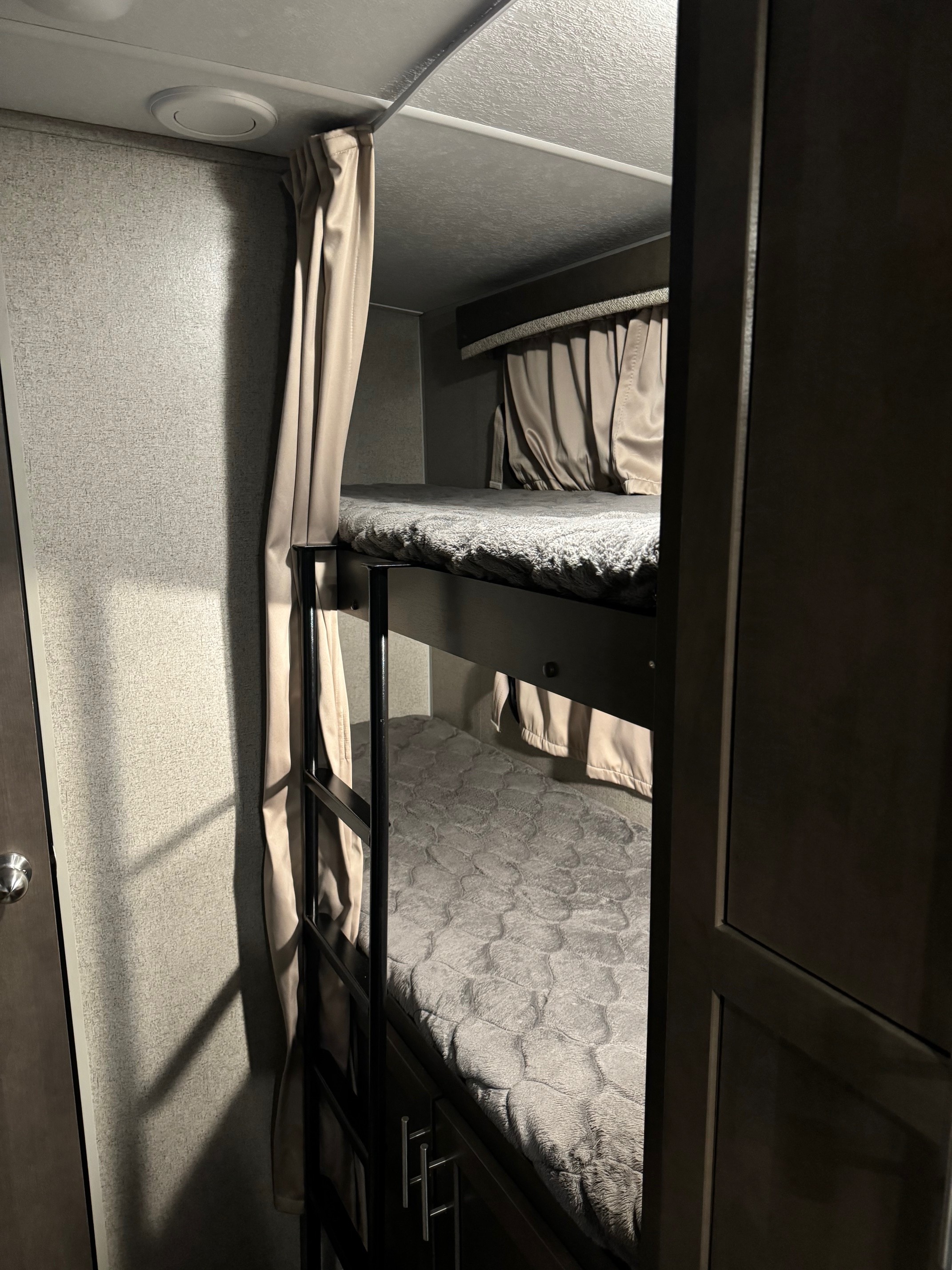 This RV rental features two stacked bunk beds with grey blankets and privacy curtains, offering a cozy sleeping space.. Forest River Rockwood Mini Lite 2020