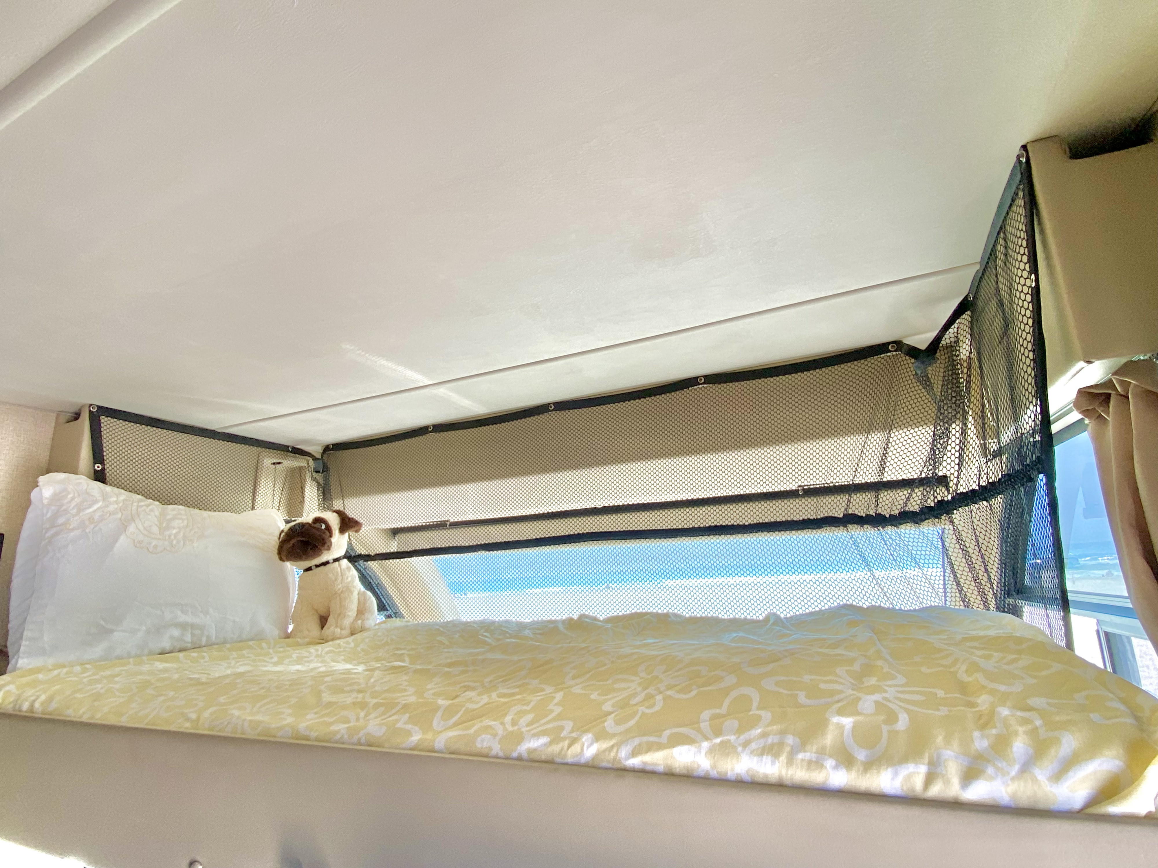 Cozy RV rental bunk with yellow bedding, white pillow, & pug toy. Mesh safety net offers clear view outside.. Thor Axis 2017