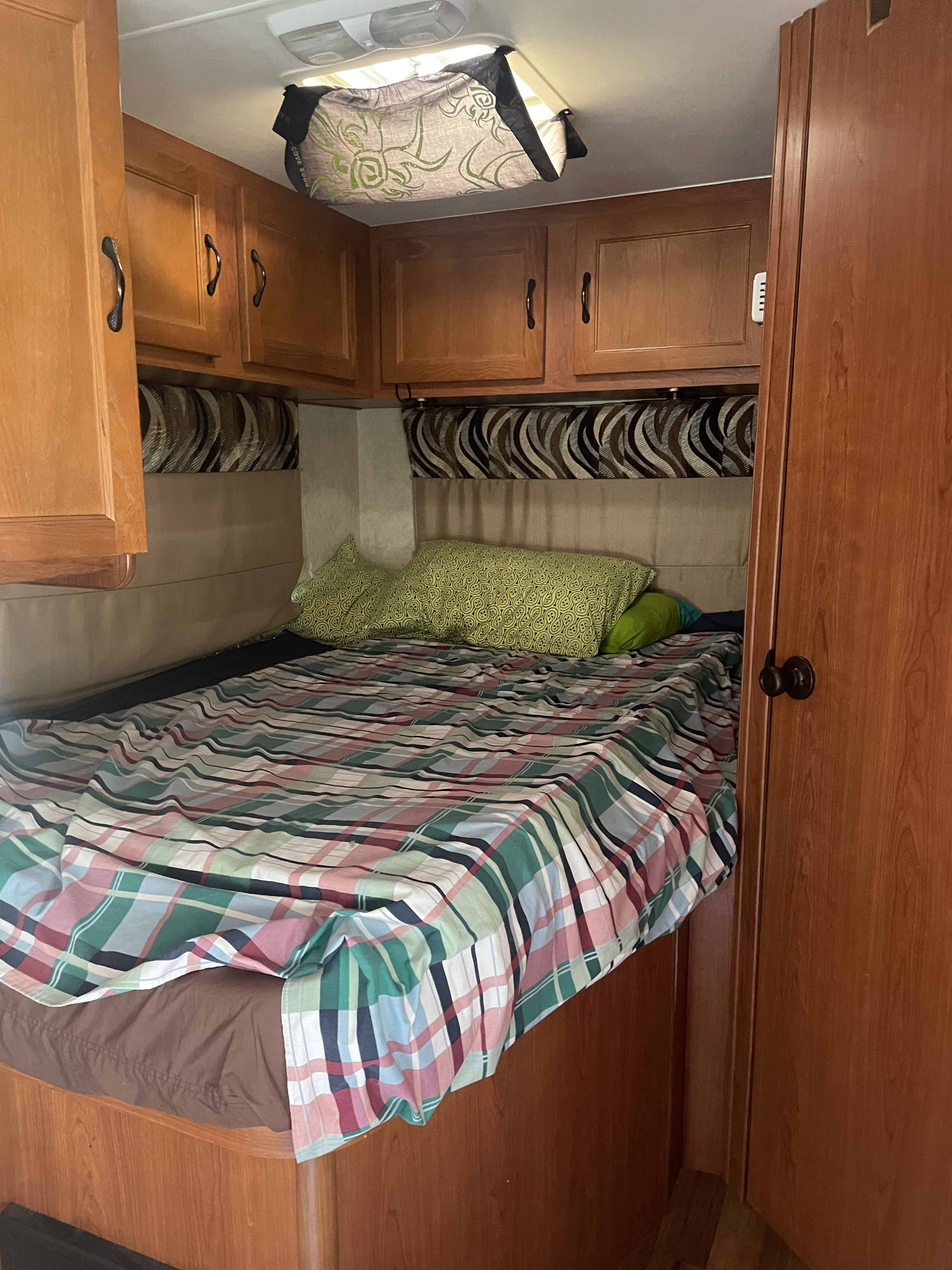 This inviting RV rental bedroom features a comfy bed with plaid bedding, green pillows, and practical wood storage.. Ford Ford E350 2013