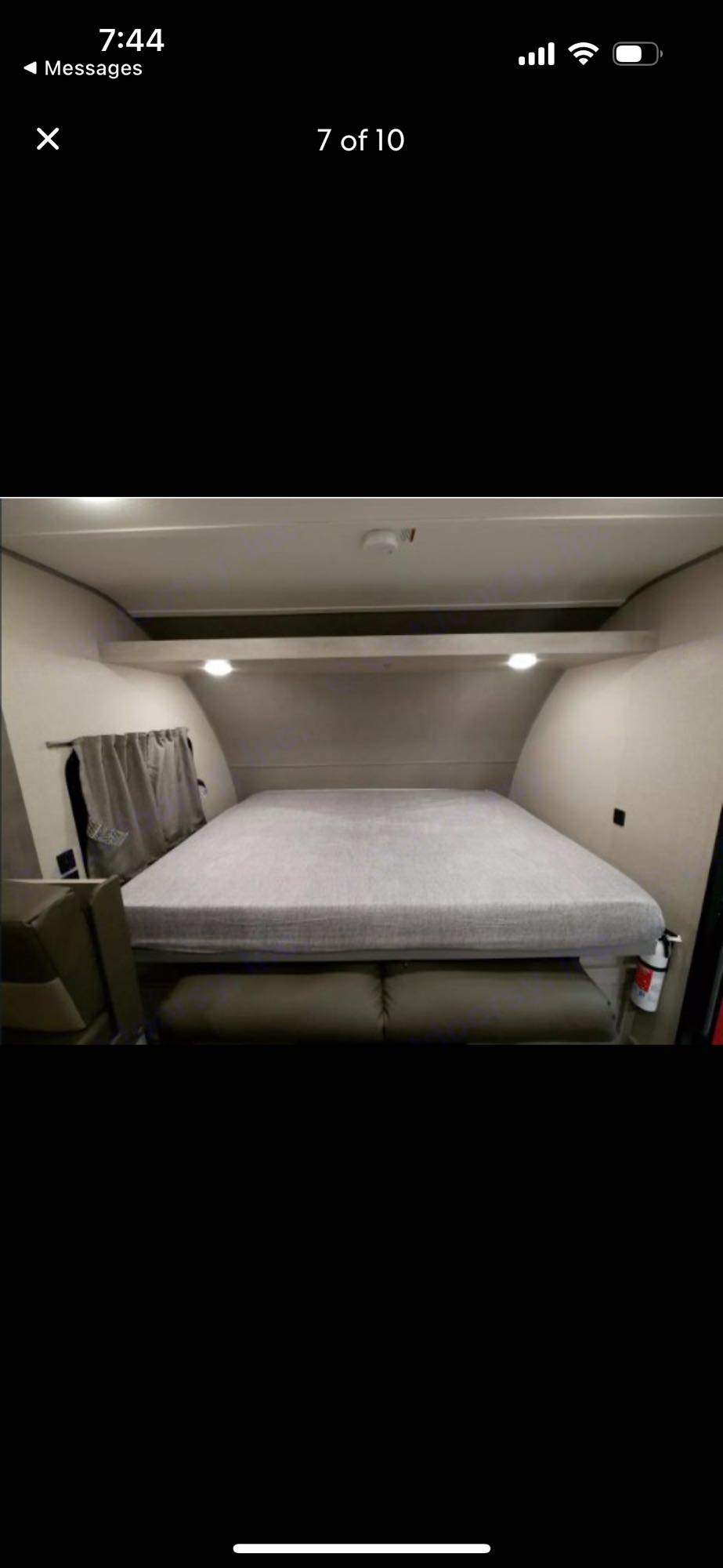 RV rental: Interior shows a light grey bed over a sofa, with a shelf above and window curtains. Fire extinguisher visible.. Forest River Aurora Bunkhouse 2022
