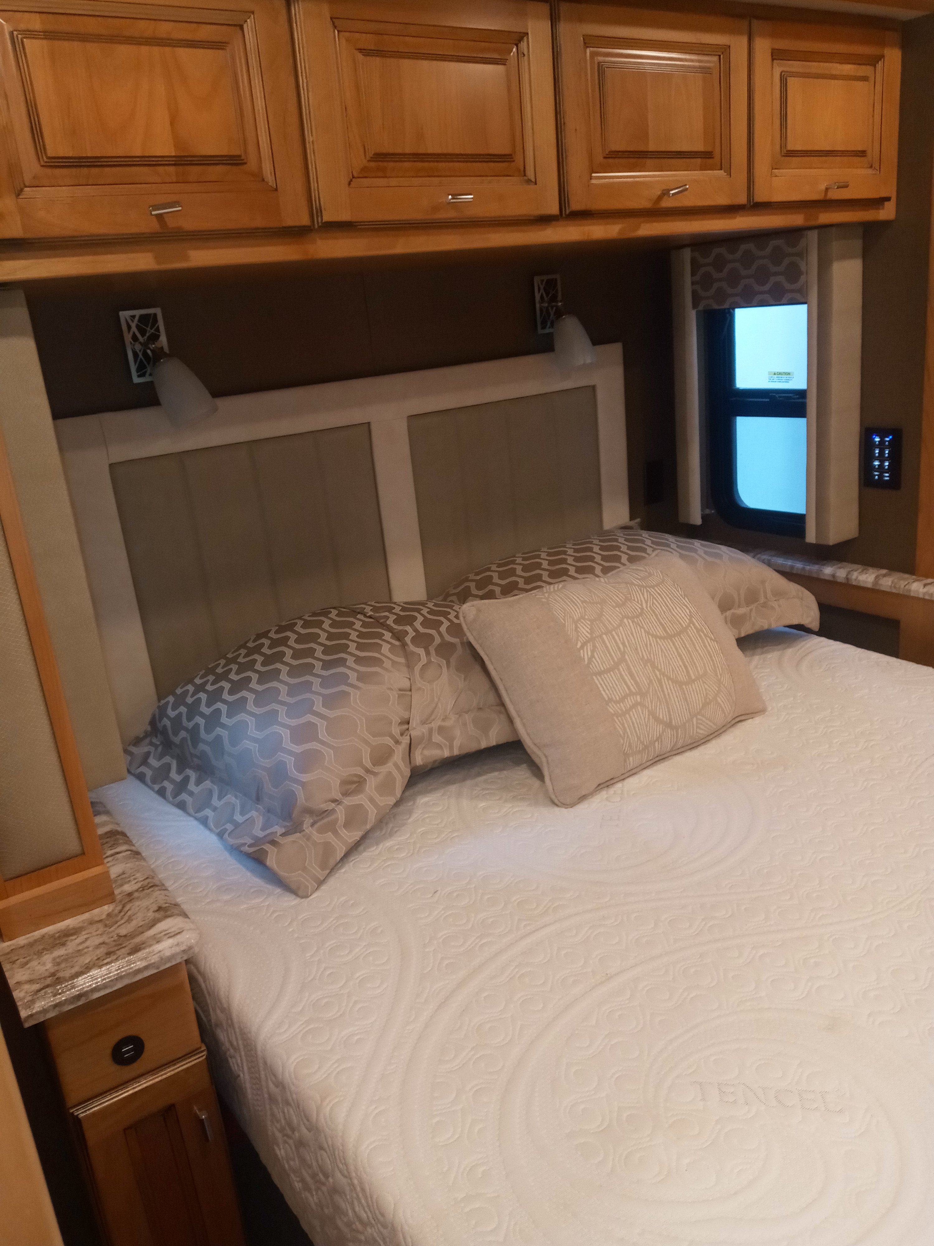 RV rental: a comfortable bedroom featuring an upholstered headboard, patterned pillows, wood cabinets, and reading lights.. Tiffin Open Road Allegro 36 foot 2019