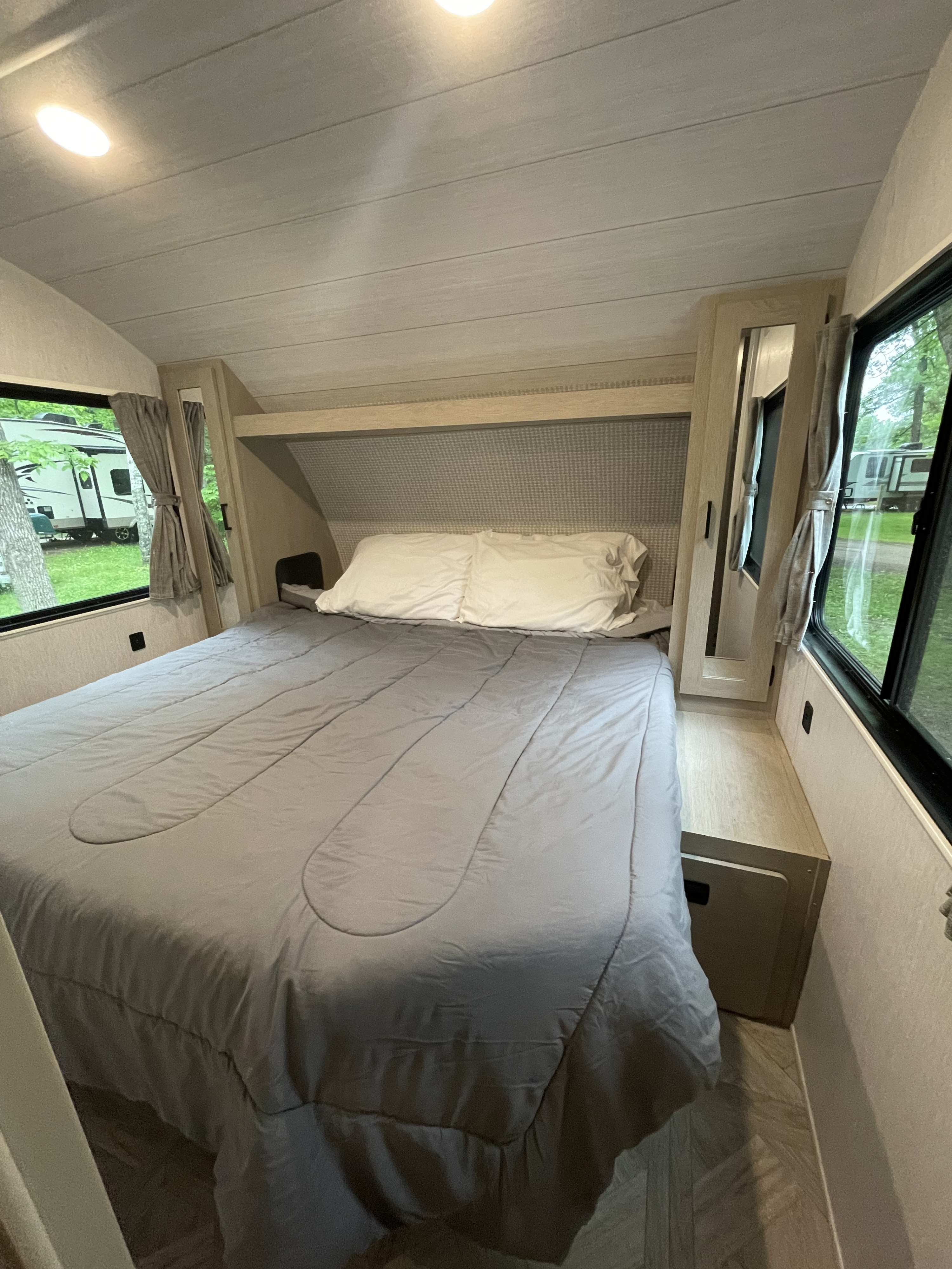 Inside an RV rental, a comfy bedroom features a large bed with grey bedding, light wood interior, and scenic window views.. Forest River Salem Cruise Lite Platinum 2024