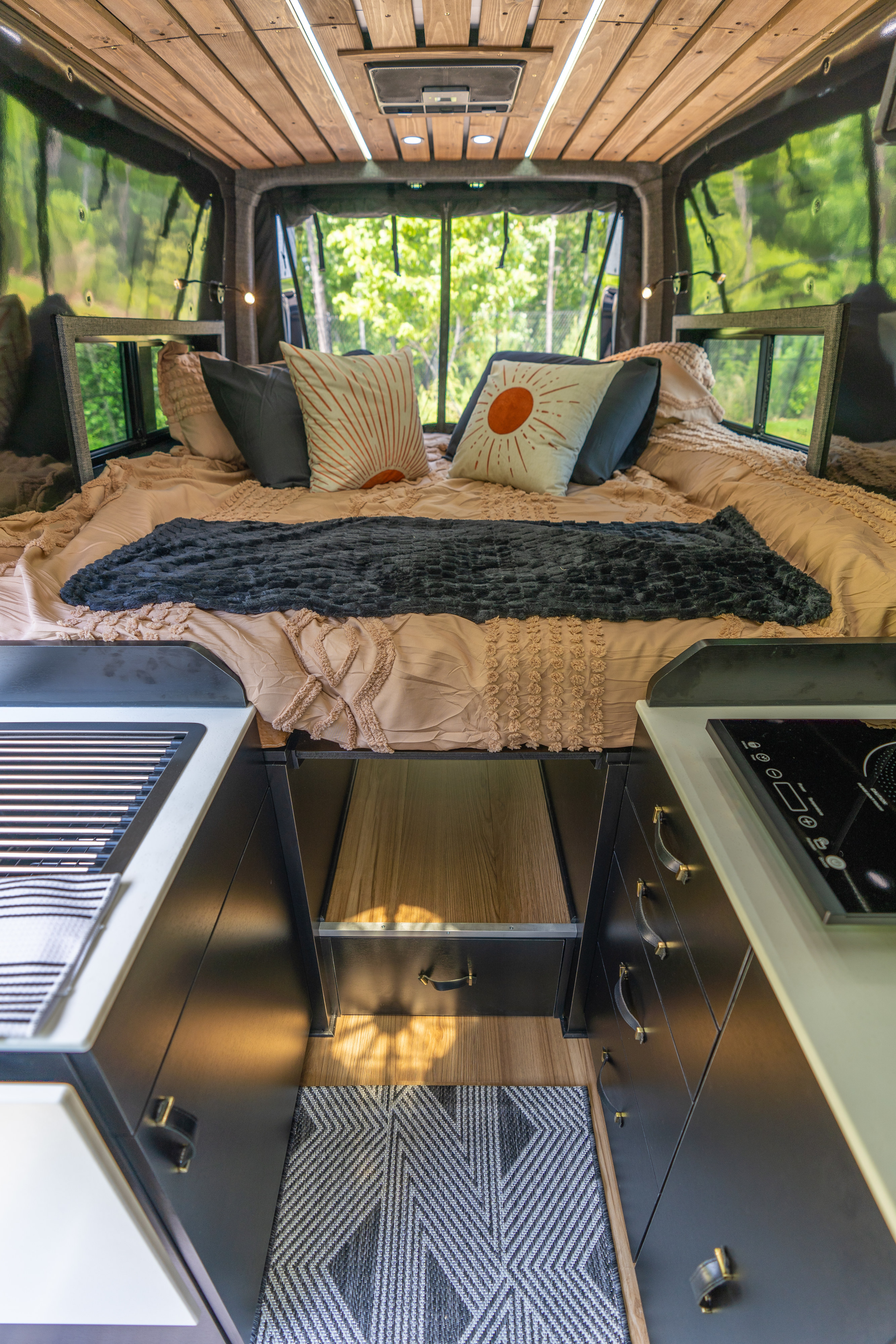 This rv rental offers a well-appointed interior with a cozy bed, compact kitchen, and wood-paneled ceiling, viewed from the front.. Mercedes-Benz Sprinter 2023