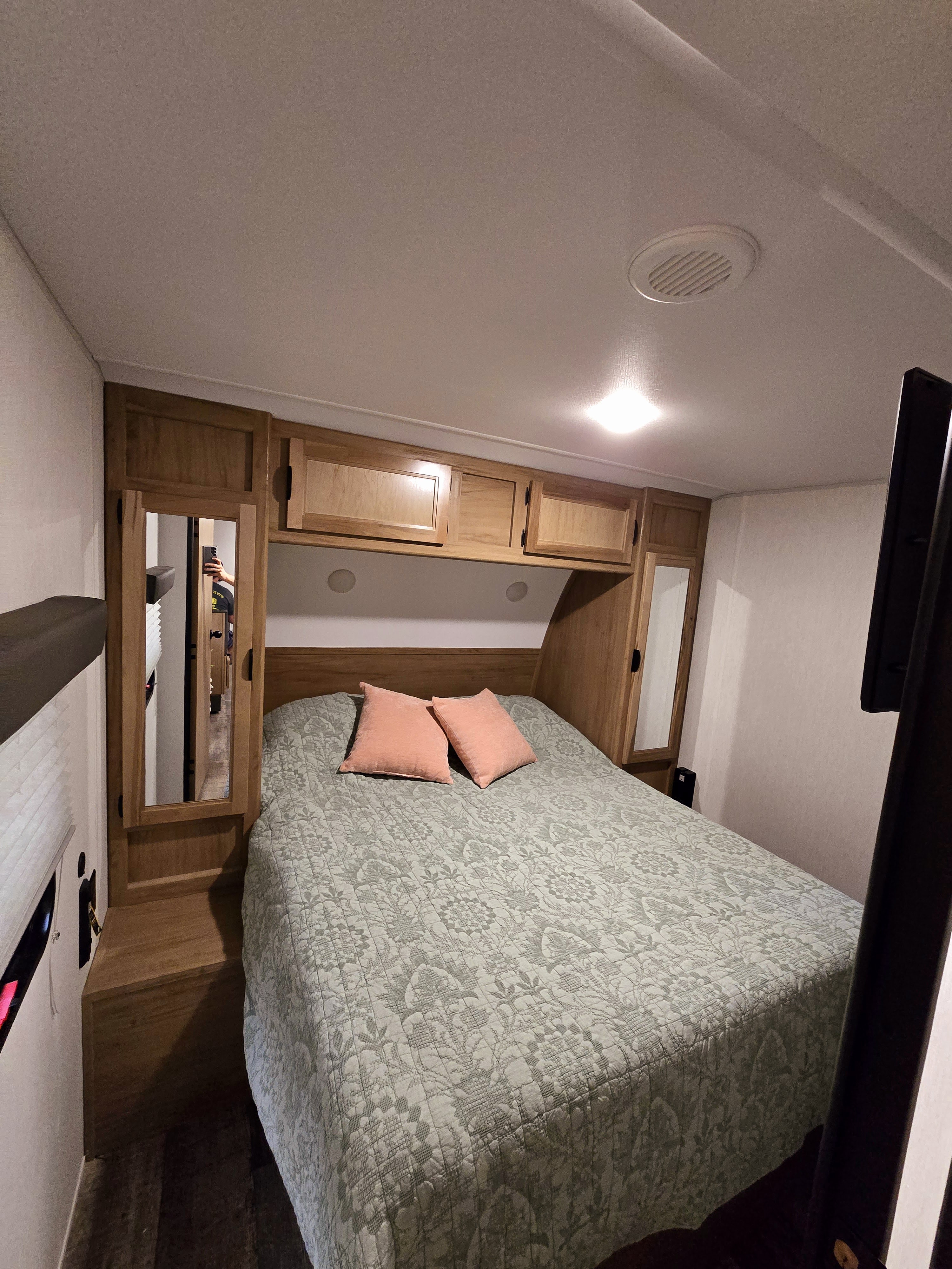 Well-appointed RV rental bedroom. Features a queen bed with patterned quilt, wooden cabinets, and ceiling light/vent.. Forest River Grey Wolf 2024