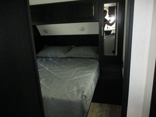 View inside an RV rental bedroom showing a bed with grey linens, dark cabinets, and a mirrored wardrobe.. Forest River Cherokee Grey Wolf 2022