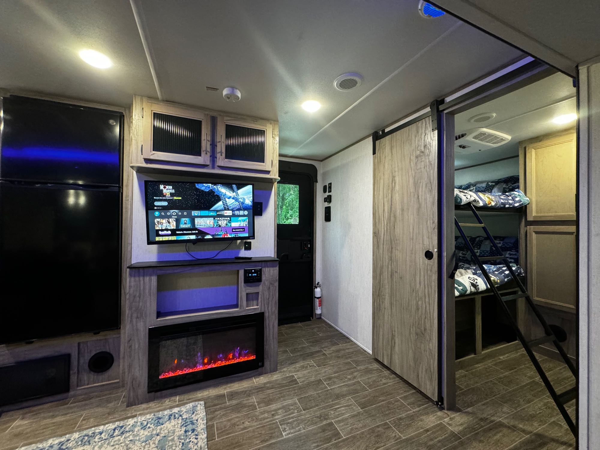 This cozy RV rental interior features an entertainment center with a TV and fireplace, plus a bunkhouse area, offering a comfortable living space.. Forest River Cherokee Alpha Wolf 2022