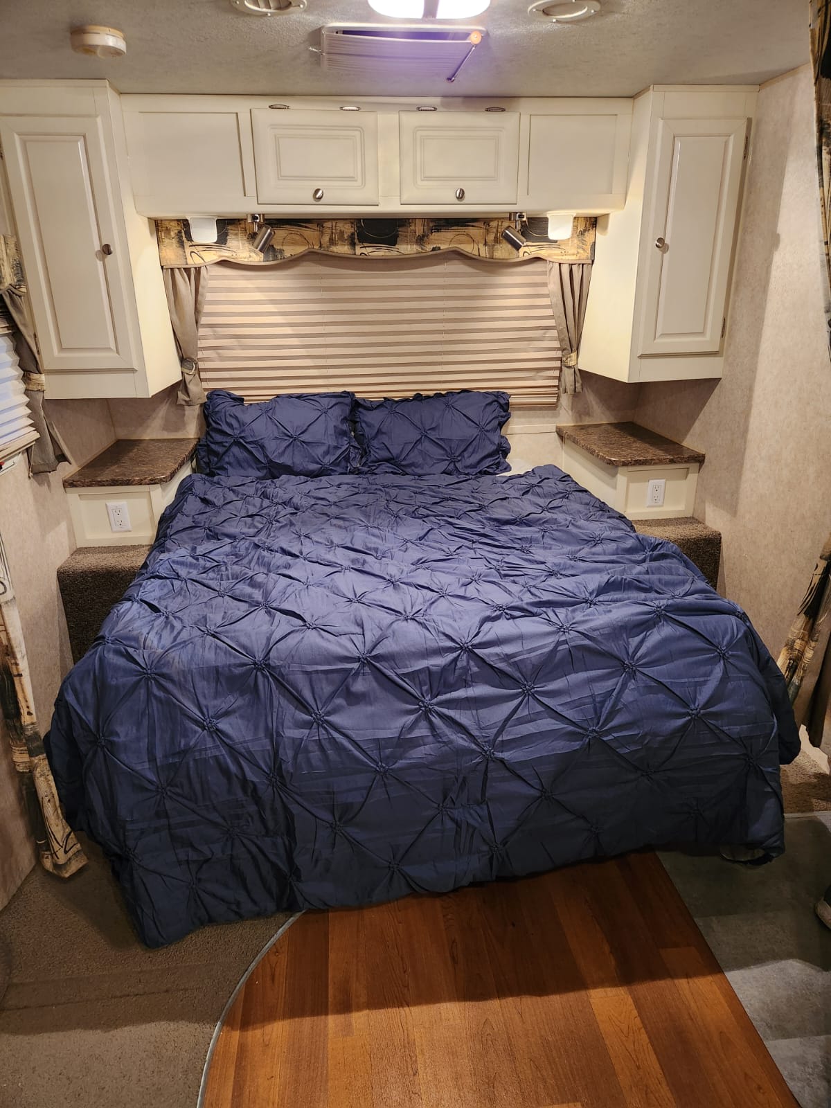 Spacious RV rental bedroom with a blue tufted bed, overhead cabinets, and nightstands. Ideal for comfortable travel.. Forest River Rockwood Ultra Lite 2010