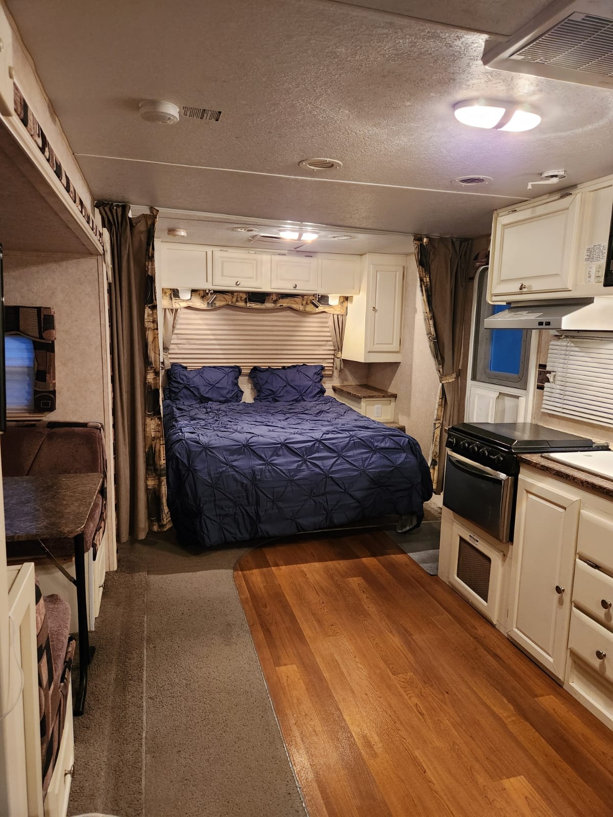 This RV rental interior features a bed with blue covers, a full kitchen with an oven, and a cozy dinette setup.. Forest River Rockwood Ultra Lite 2010