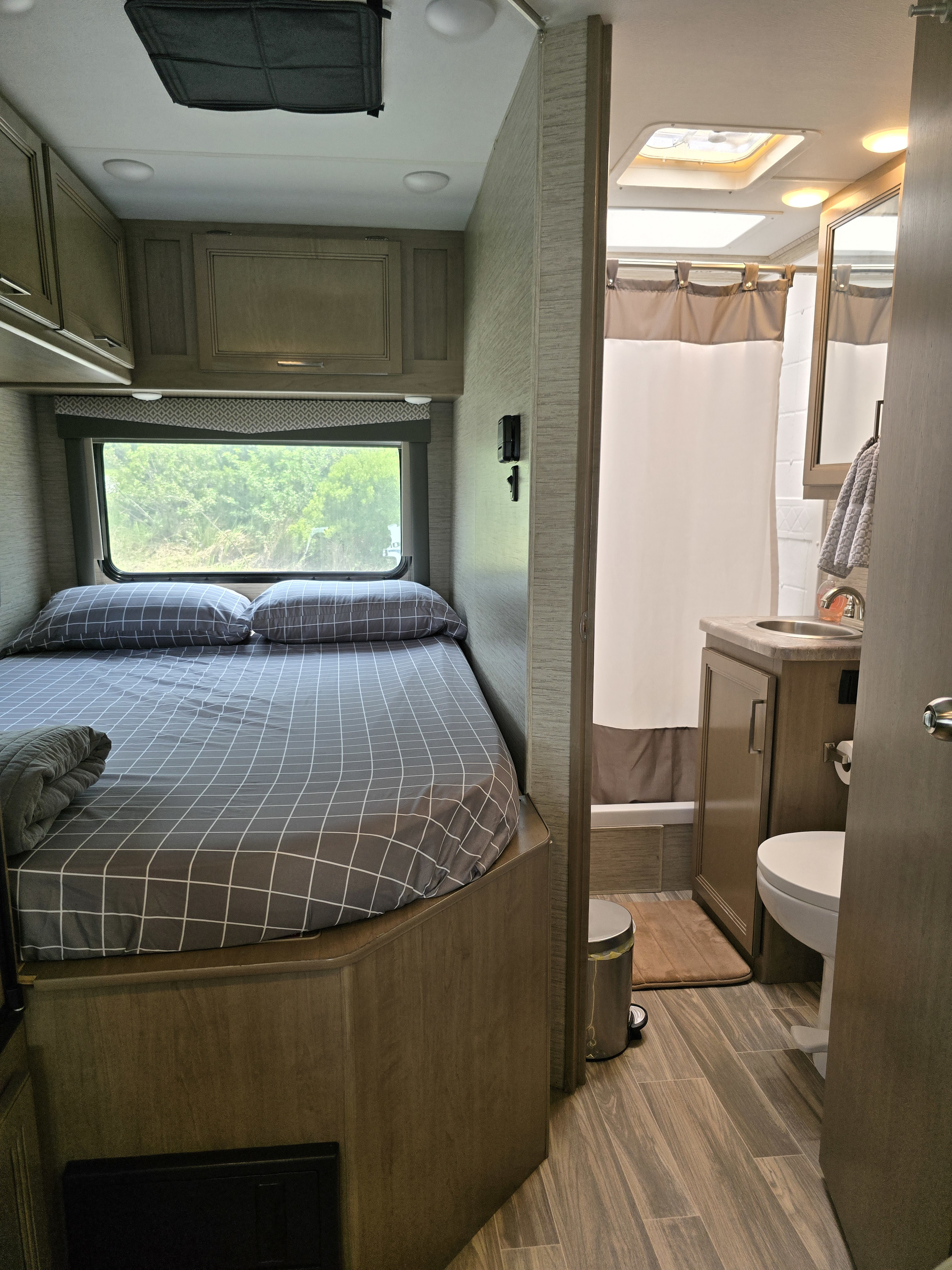 RV rental interior showcasing a cozy bedroom with grid bedding and a compact, fully equipped bathroom, perfect for travel comfort.. Thor Four Winds 2022