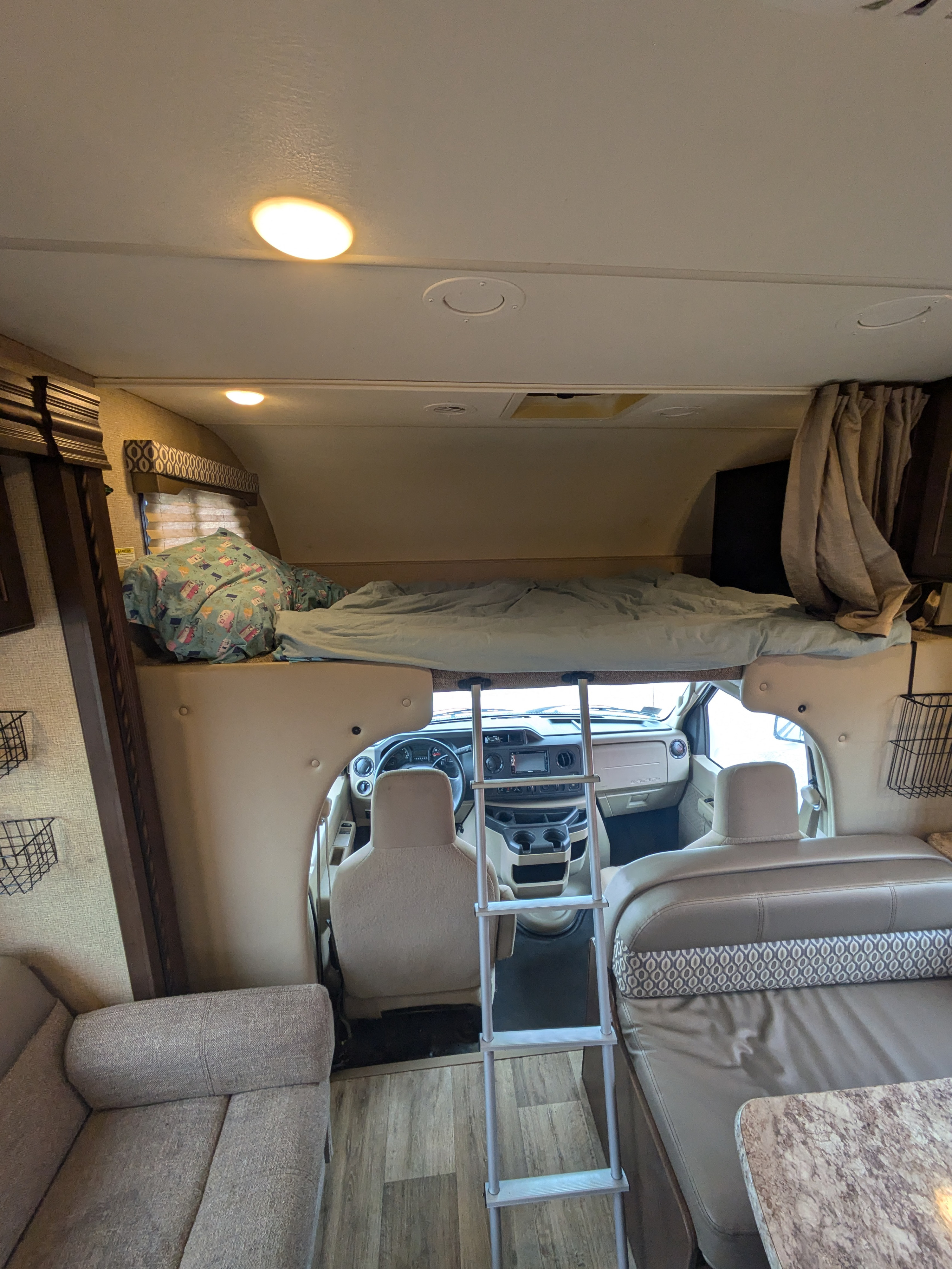 Inside an RV rental: a cozy overhead bunk with ladder, front cab, and comfortable living area with seating.. Thor Freedom Elite 2018