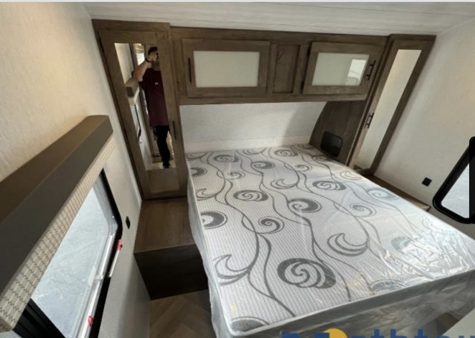 Explore this RV rental's primary bedroom, featuring a large bed, overhead cabinets, mirrored wardrobes, and a window.. Forest River Wildwood 2022