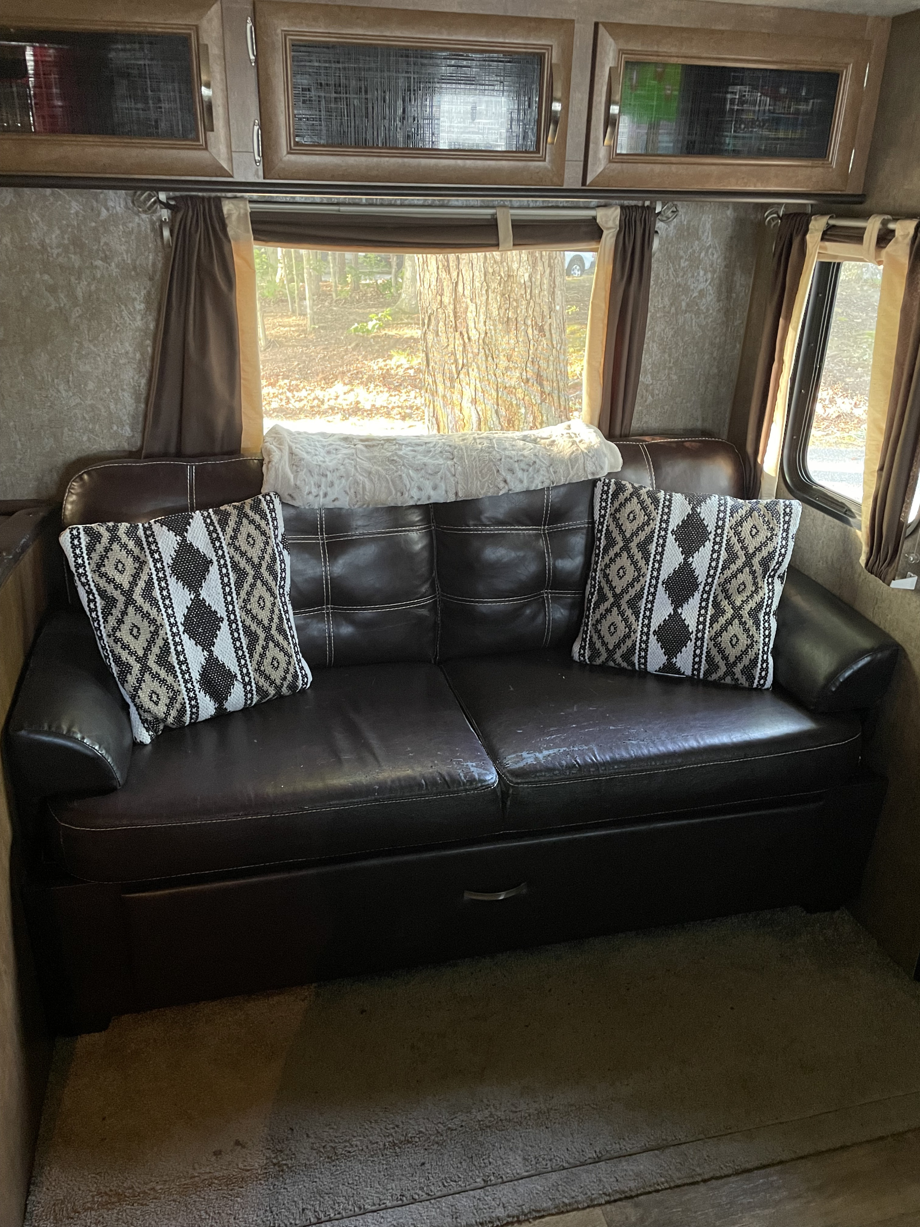 Inside a cozy RV rental: a plush leather sofa with patterned pillows, overhead cabinets, and bright windows.. Forest River Wildwood 2016
