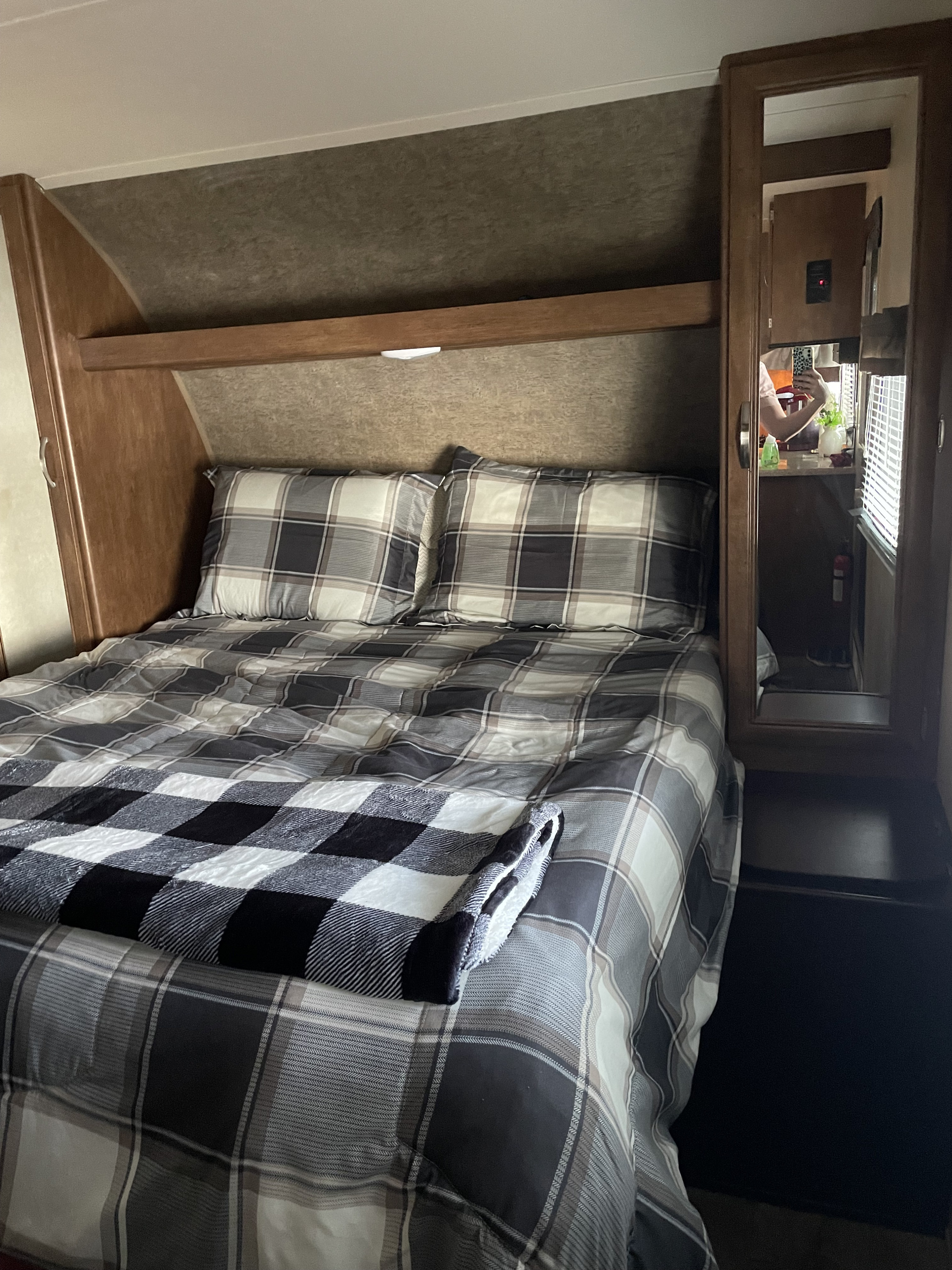 Cozy RV rental bedroom featuring a plaid bed with built-in storage. The mirror reveals a compact mobile living space.. Forest River Wildwood 2016