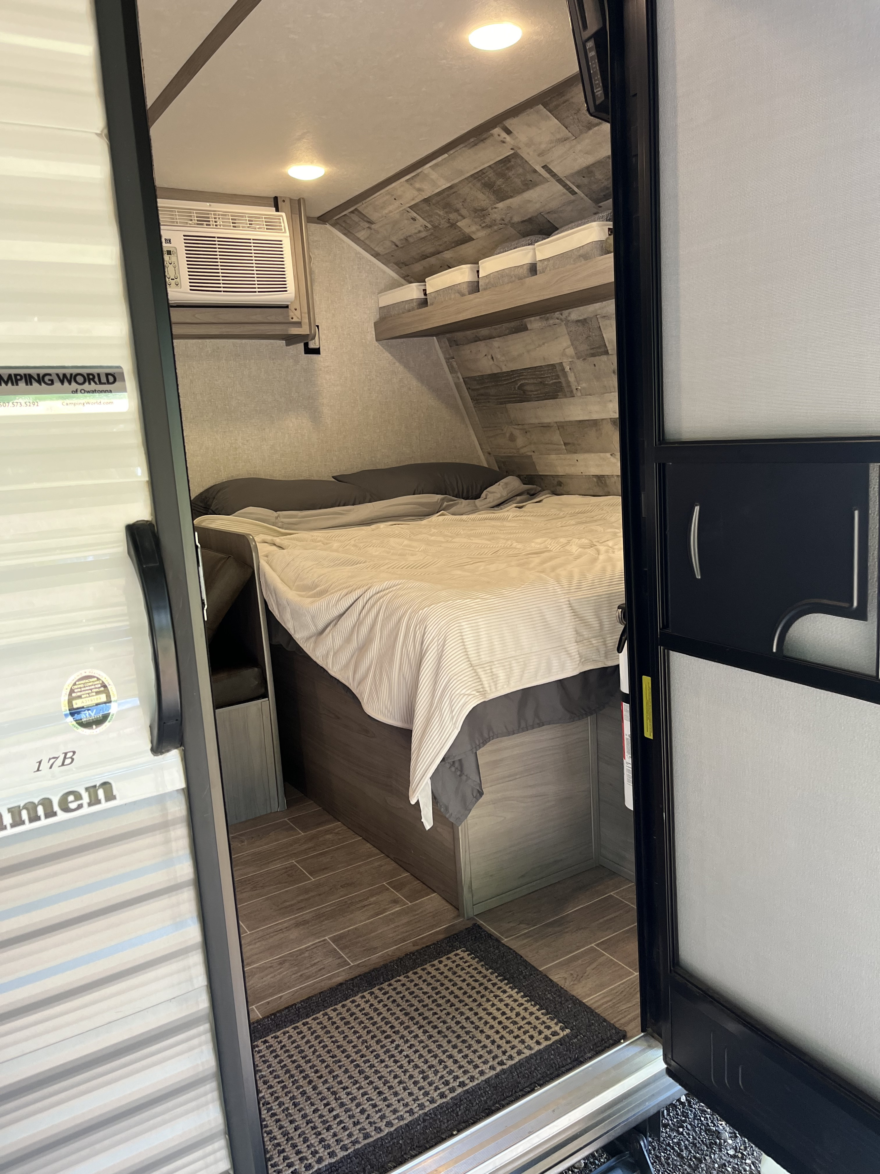View of a modern RV rental interior, showing a comfortable bed, wall-mounted AC unit, and storage shelves.. Dutchmen Coleman Lantern LT 2022