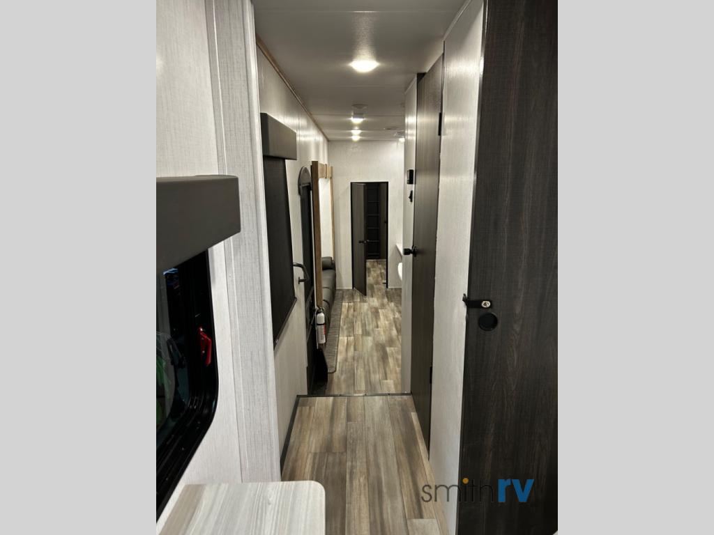 Inside a modern RV rental: View down a clean hallway with light walls, dark doors, and wood-look flooring.. Heartland Bighorn 2023