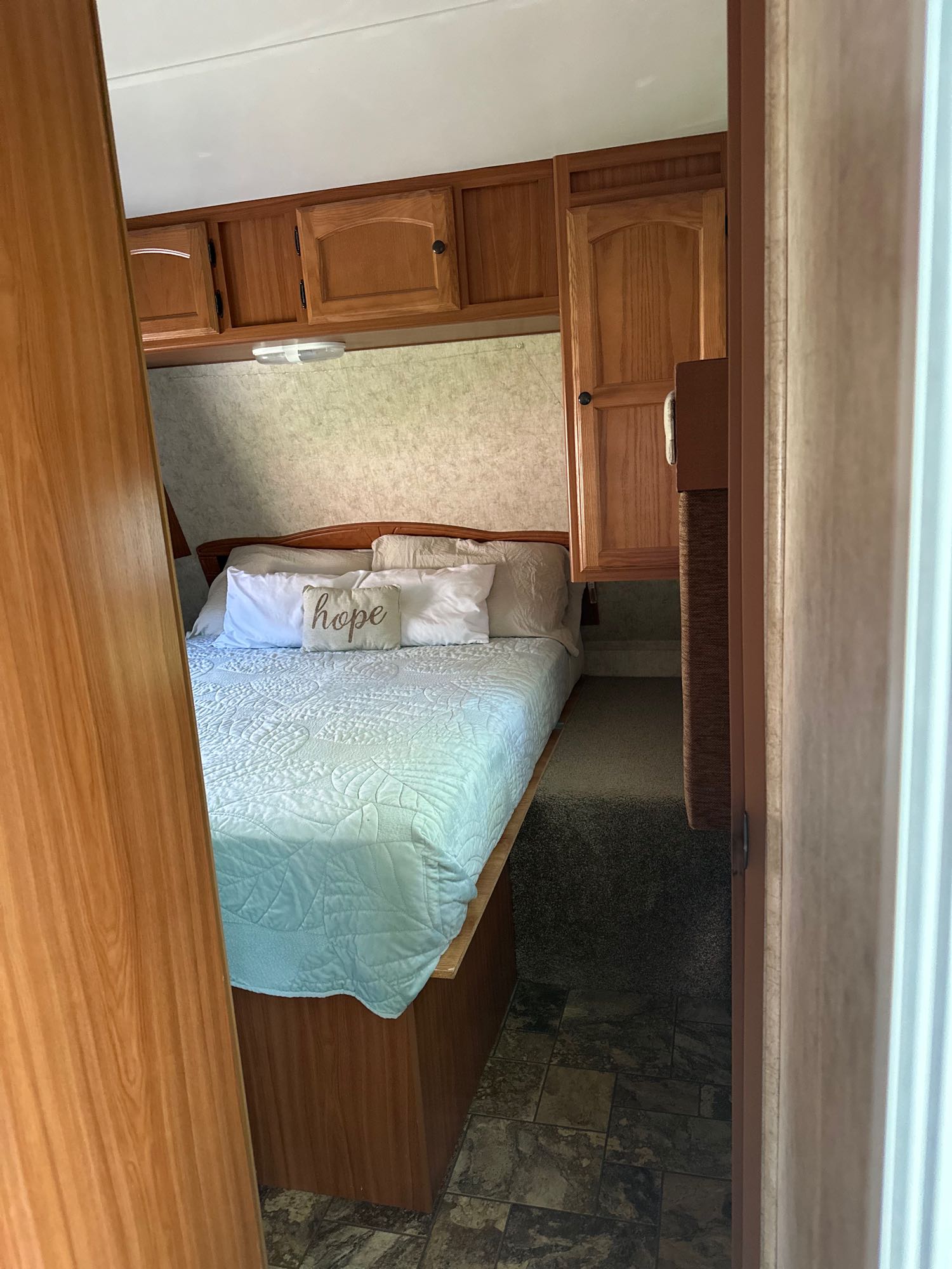A cozy RV rental bedroom featuring a bed with a "hope" pillow, wood cabinets, and mixed flooring.. Four Winds Breeze SS 2010