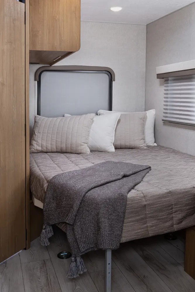 Cozy RV rental bedroom featuring a comfortable bed with neutral bedding, a throw blanket, and pillows. Compact yet inviting.. Forest River Coachmen Leprechaun 2024