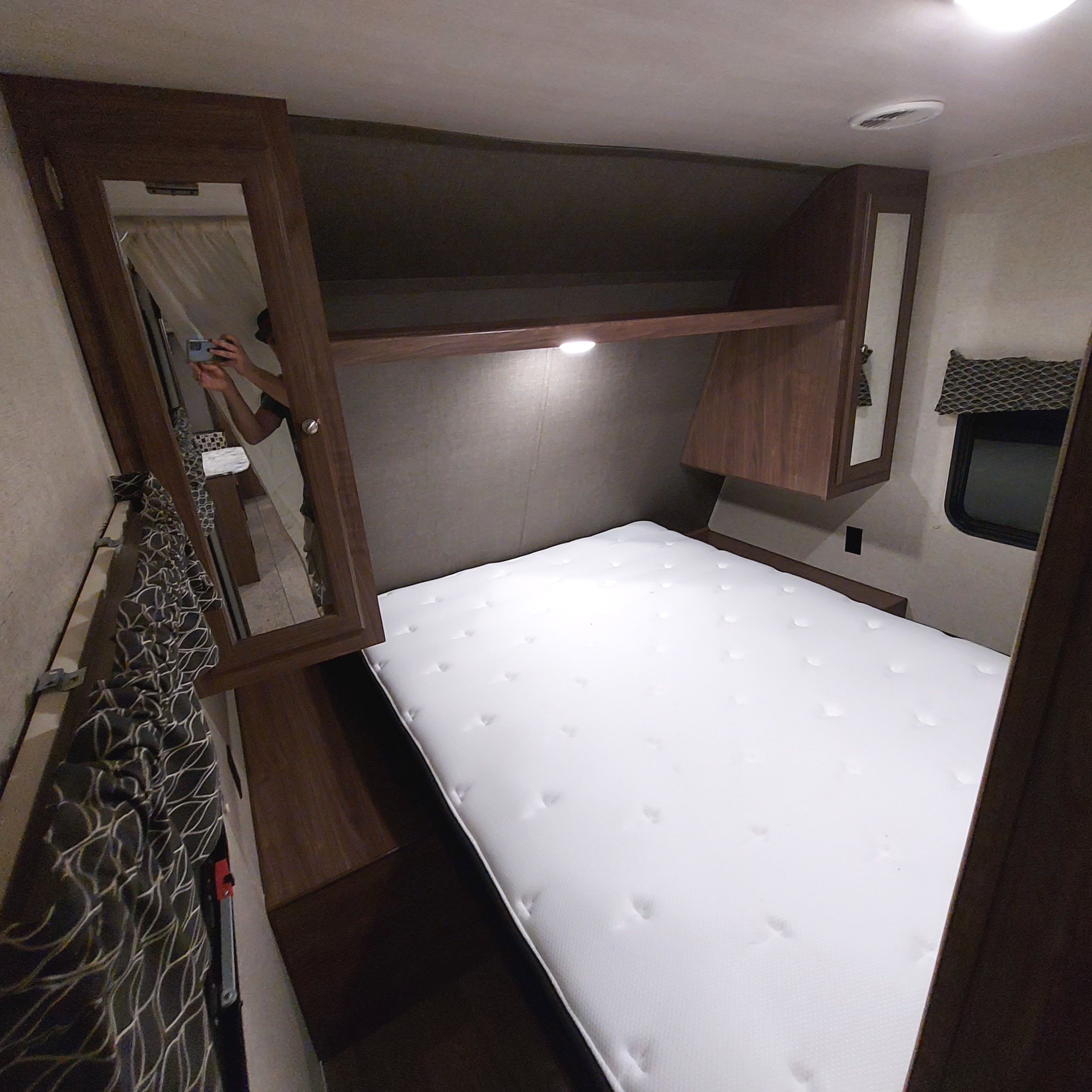 RV rental bedroom interior: clean white mattress, dark wood overhead storage, mirrored cabinet, and a window for comfort.. Heartland Prowler Lynx 2018