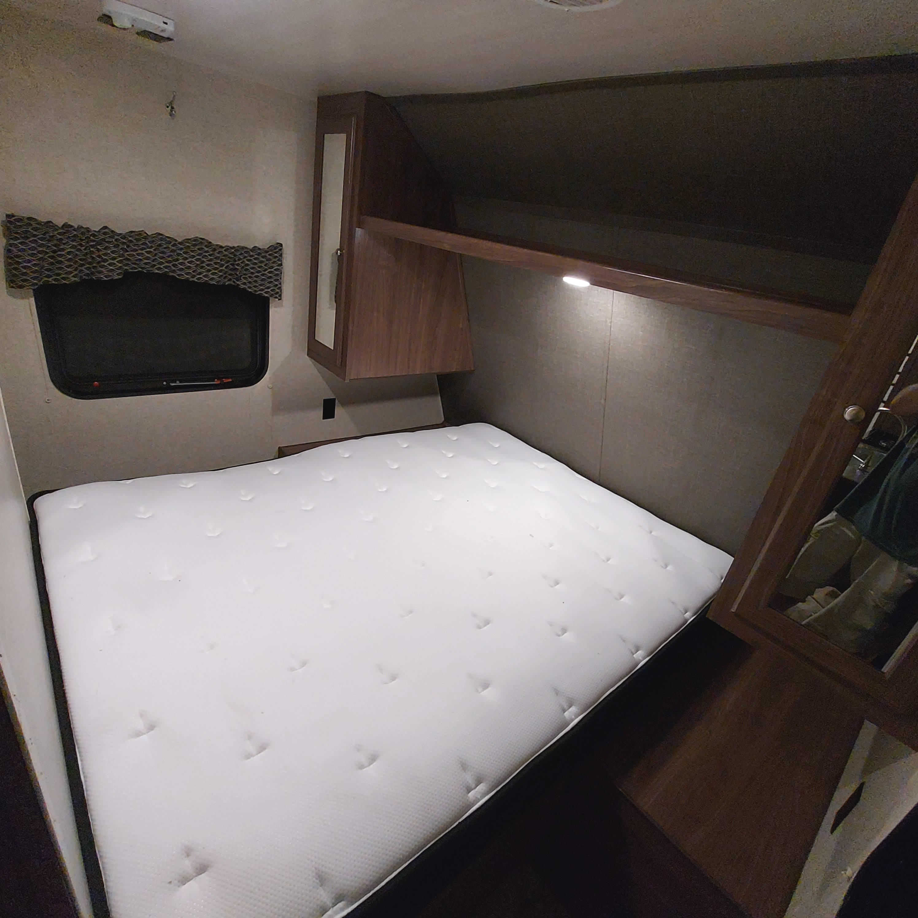 This RV rental bedroom features a comfortable white mattress, overhead cabinets, a window, and closet space, ideal for travel.. Heartland Prowler Lynx 2018