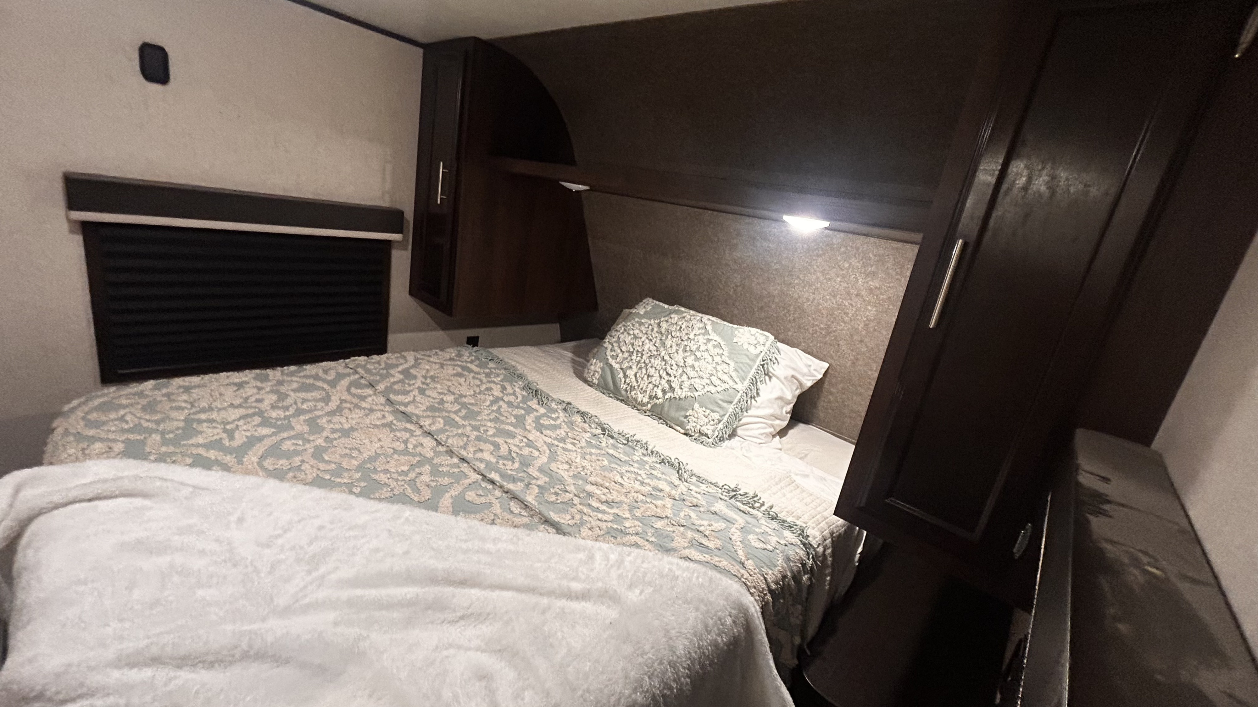 Cozy RV rental bedroom: A comfortable bed with soft bedding, window blind, and overhead storage. Jayco Jay Flight SLX 2019